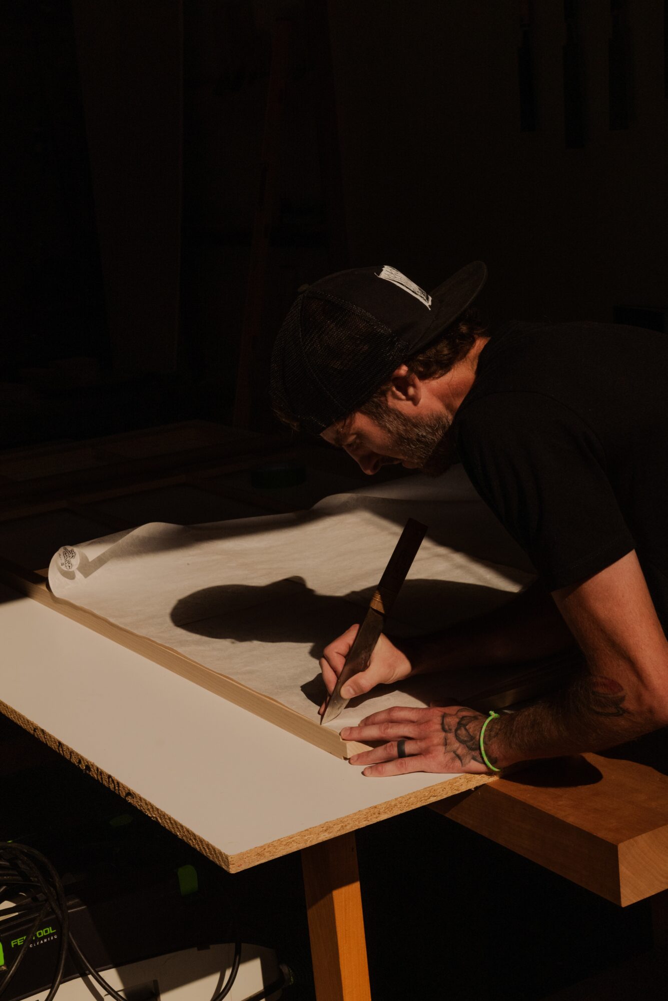 Person with a cap and tattoos signs a large white canvas in a dimly lit room.