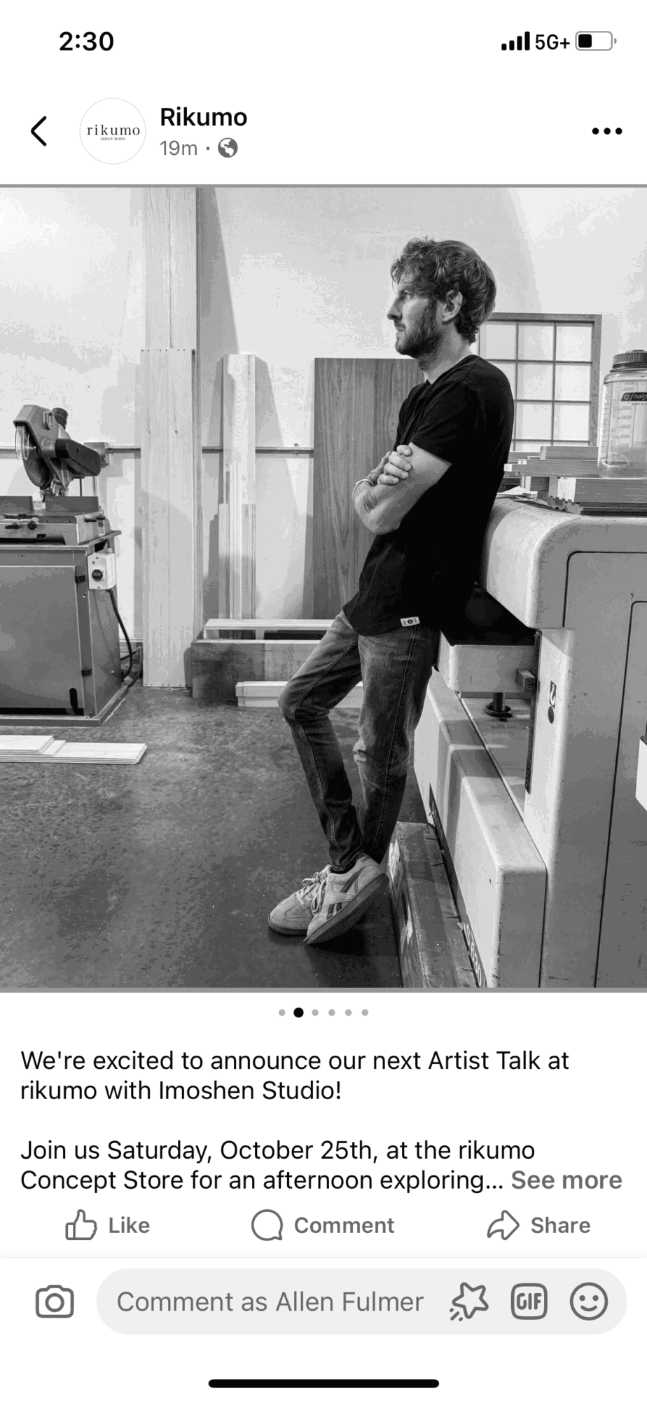 Man leaning against a counter in a store, with shelves and equipment in the background, in black and white.