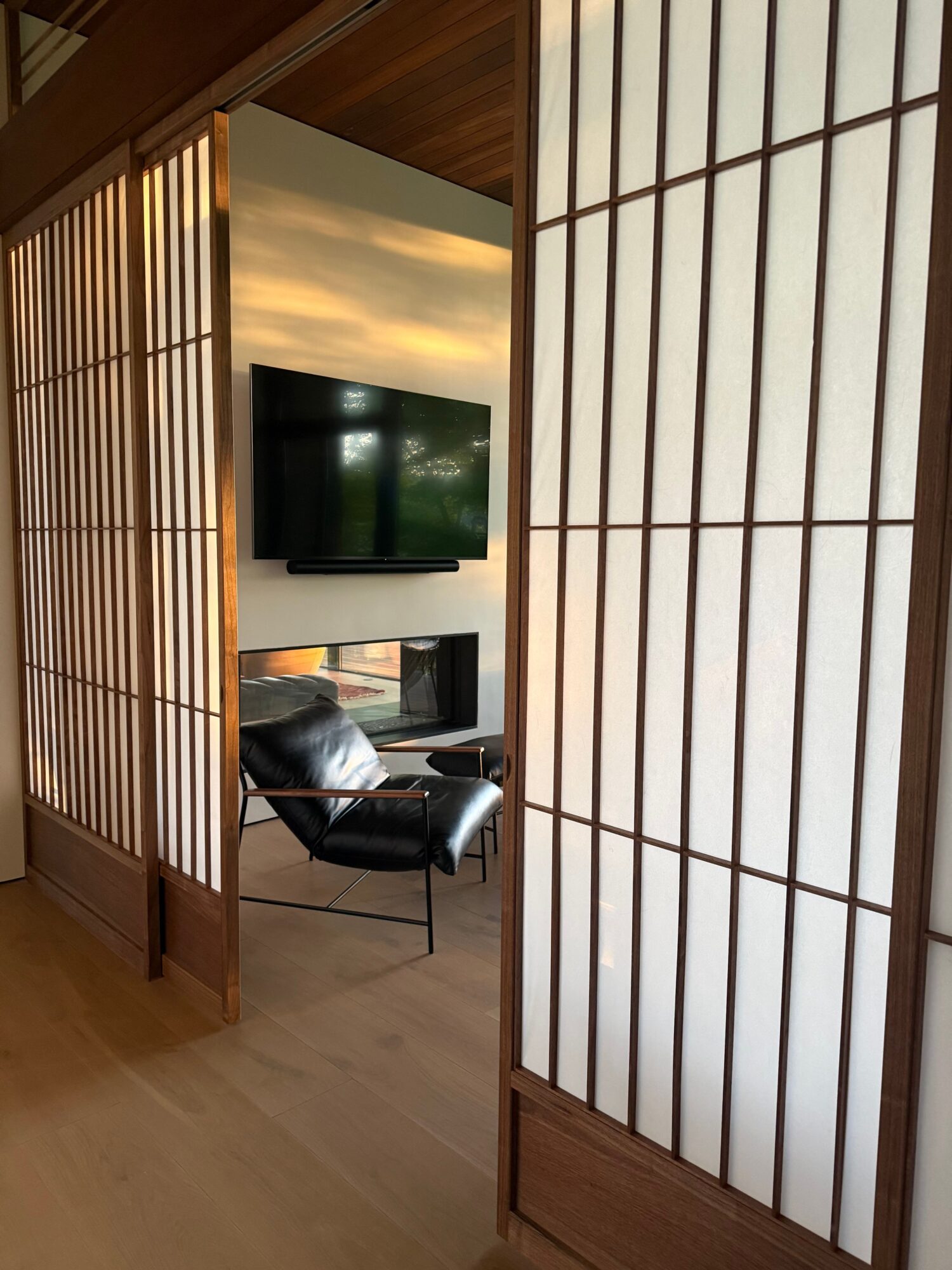 Interior room with shoji-style sliding doors, a wall-mounted TV, a chair, and a wooden floor.