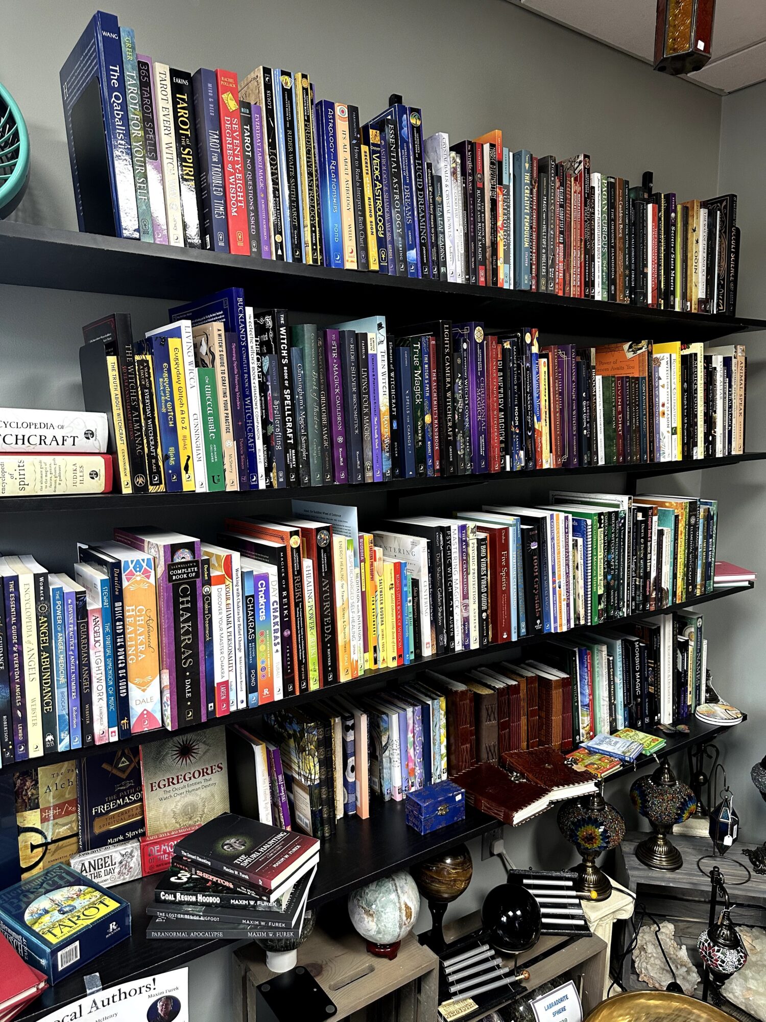 Bookshelves filled with books, some stacked horizontally, in a room with a gray wall.