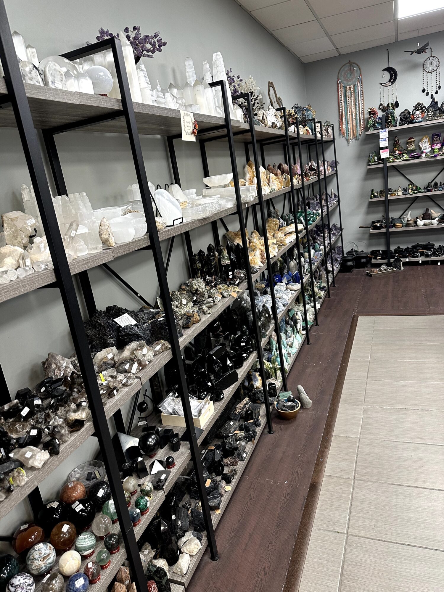 Shelves filled with various crystals, stones, and decorative objects in a store, with a tiled floor and ceiling lights.