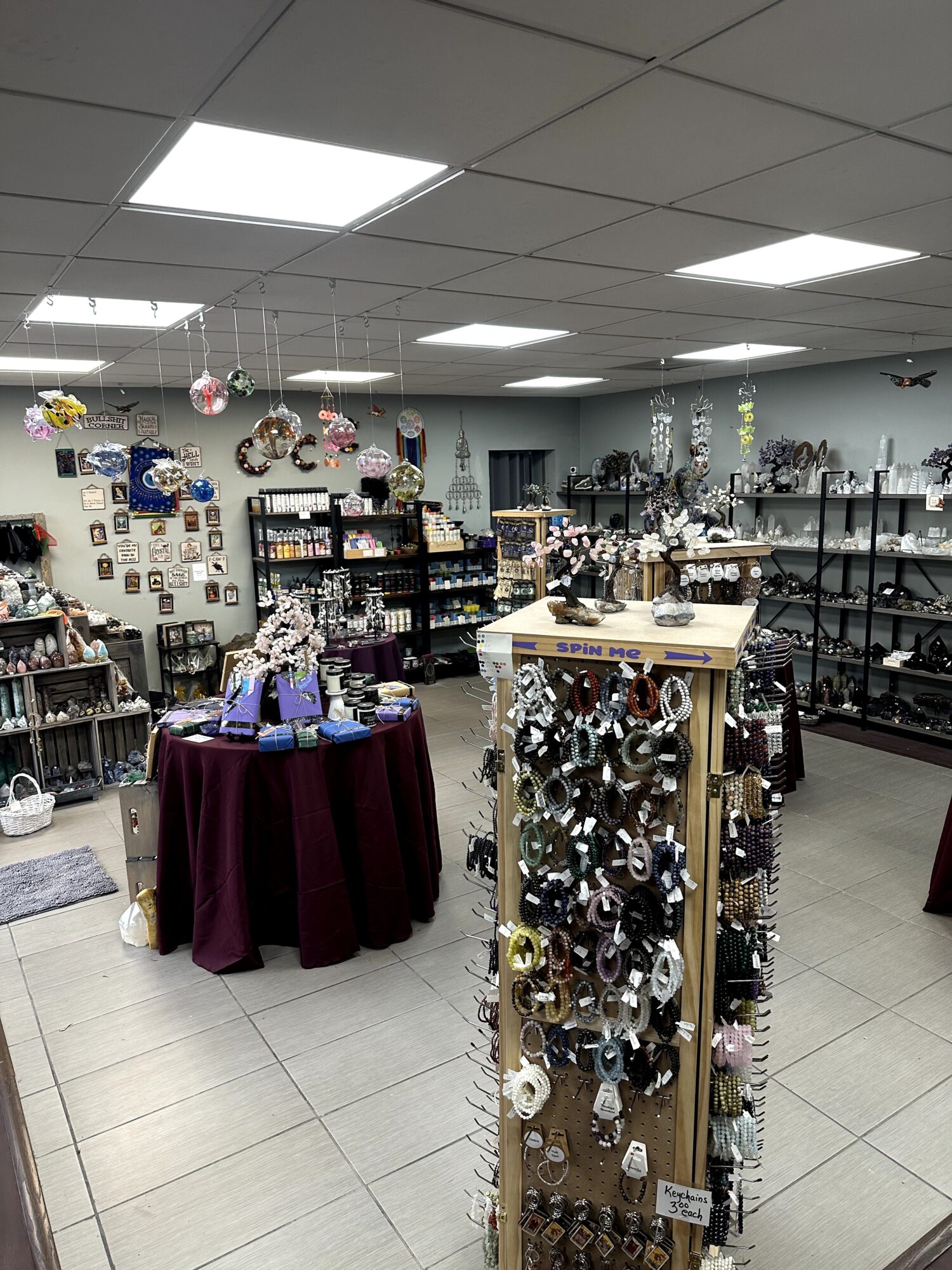Display of hanging and tabletop jewelry and ornaments in a store with shelves and decorations in the background.