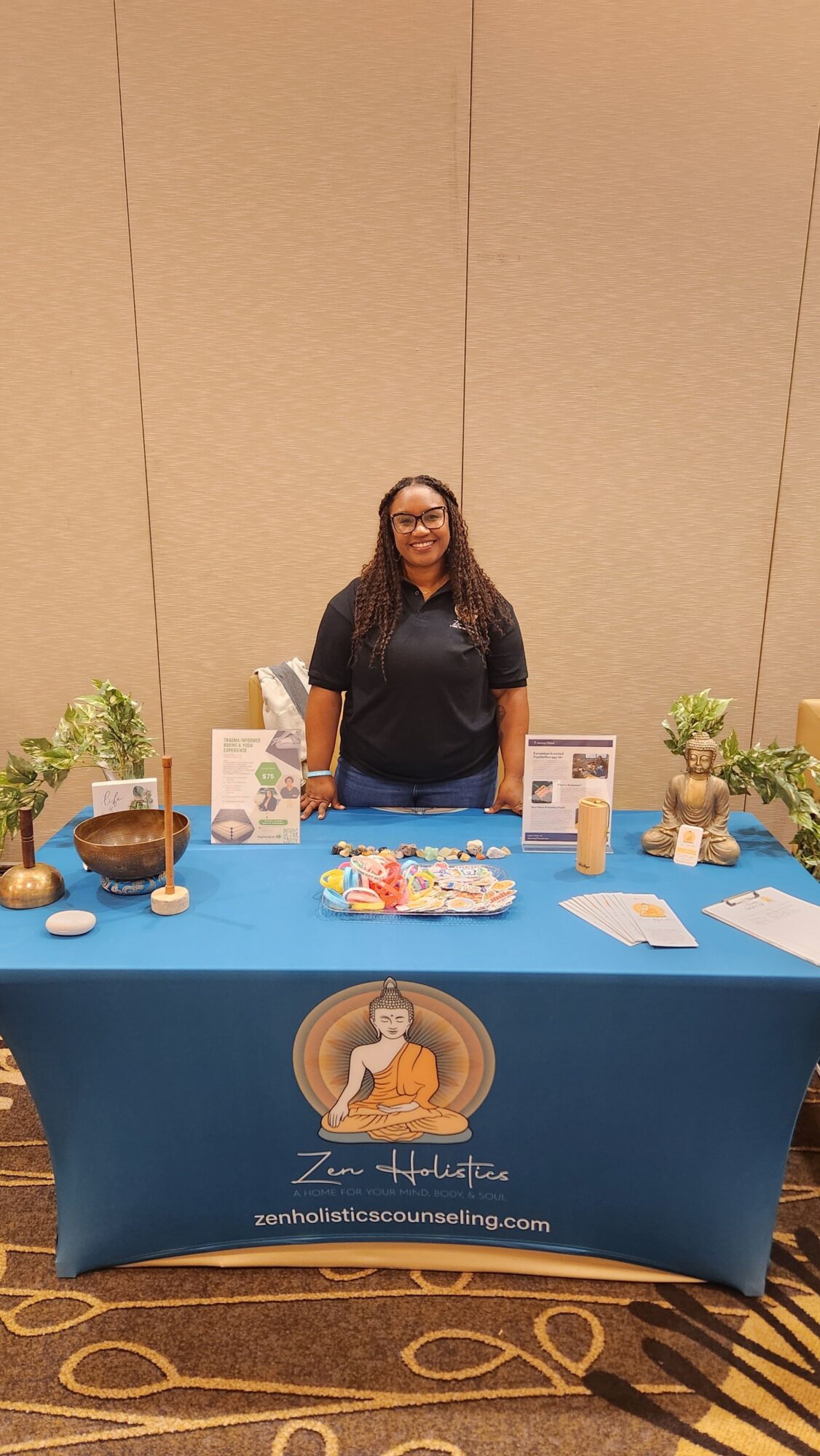 Woman standing behind a table with promotional items, in a conference room with beige walls and patterned carpet.