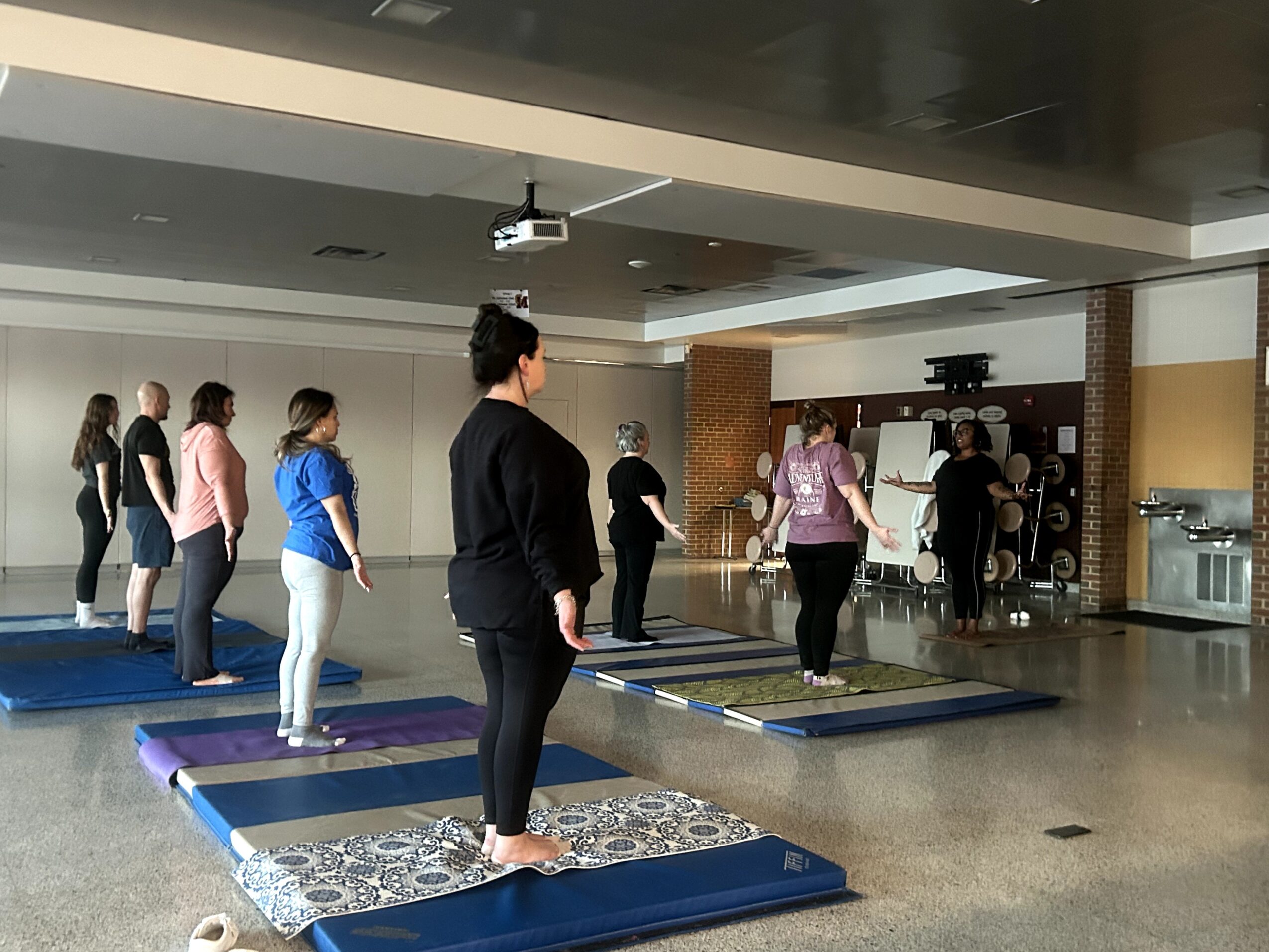 People practicing yoga on mats in a spacious indoor room with a high ceiling and large windows.