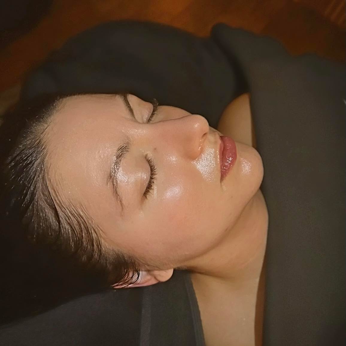 Side view of a woman with closed eyes, lying down with dark hair and smooth skin, wearing a black top.