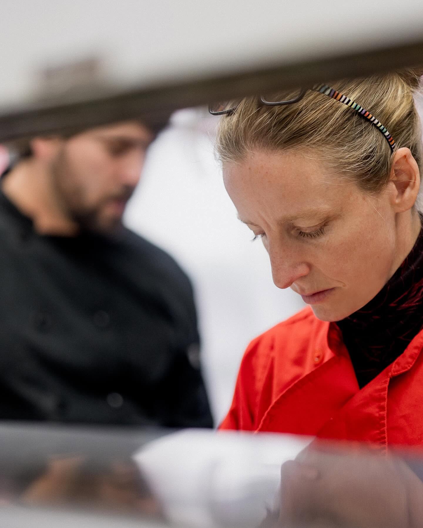 Two people, a woman in red and a man in black, focused on a task, with the woman looking downward.