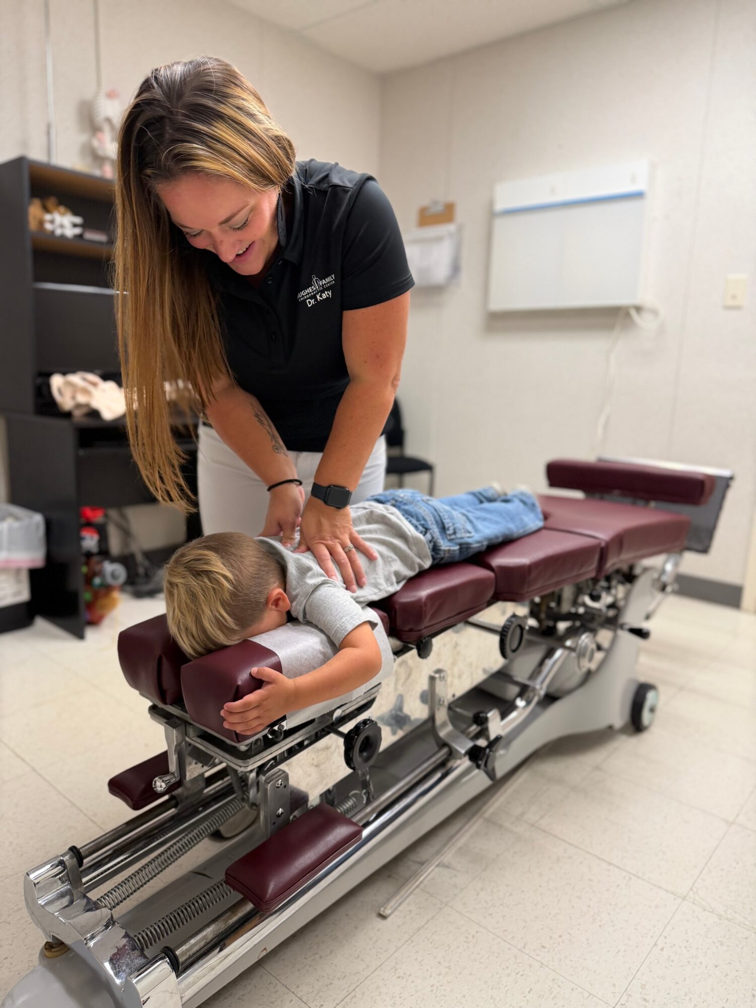 A woman adjusts a young child's position on a medical examination table in a clinical room.
