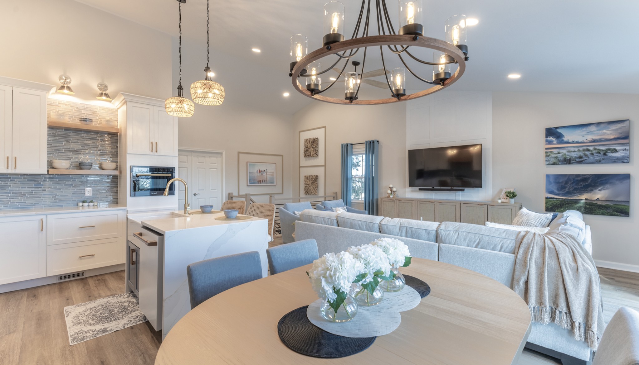 Open living and dining area with chandelier, sofa, TV, and artwork, in a bright, modern home.