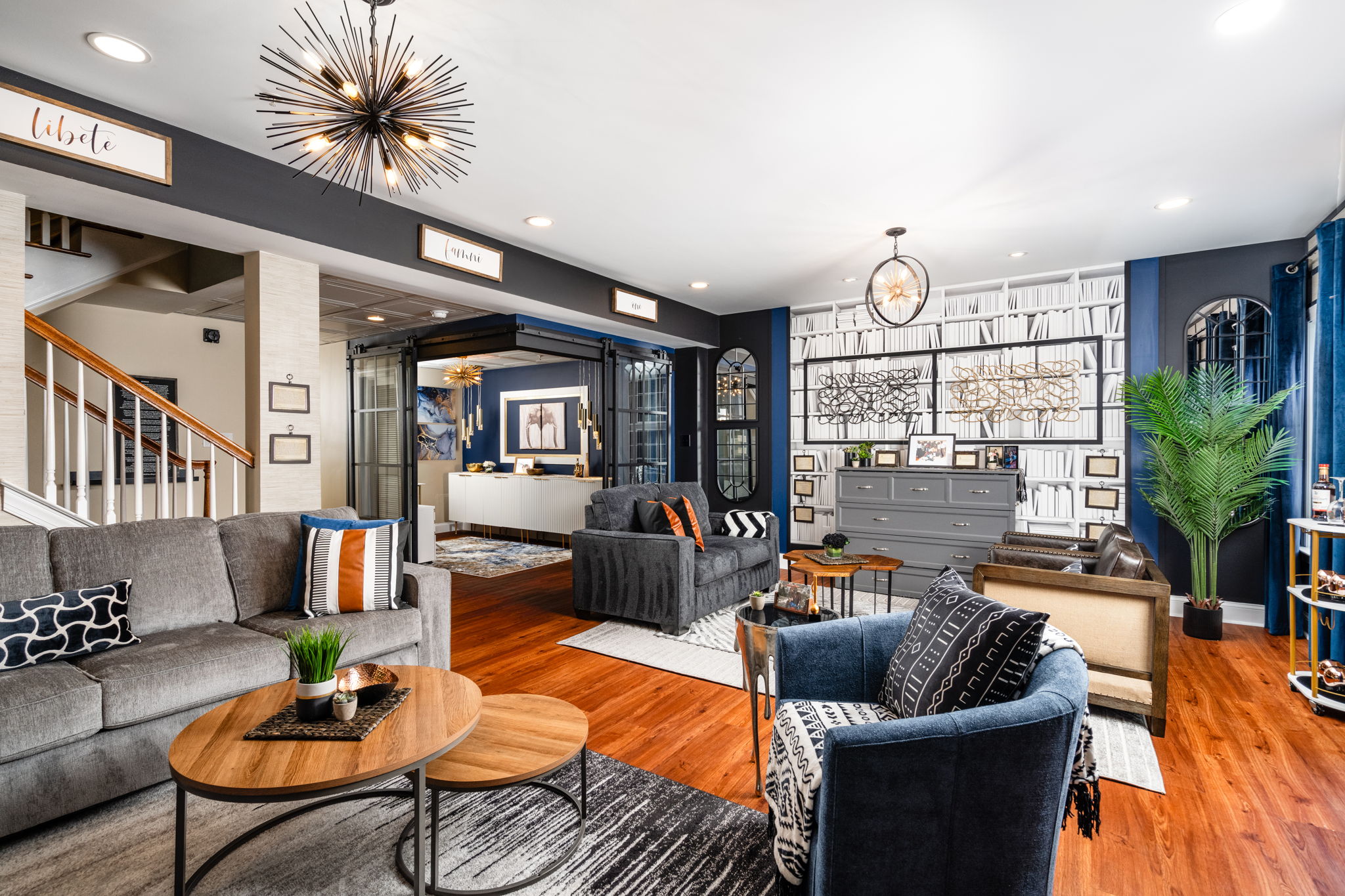 Living room with sofas, armchair, wooden coffee tables, large window, blue walls, and decorative plants.