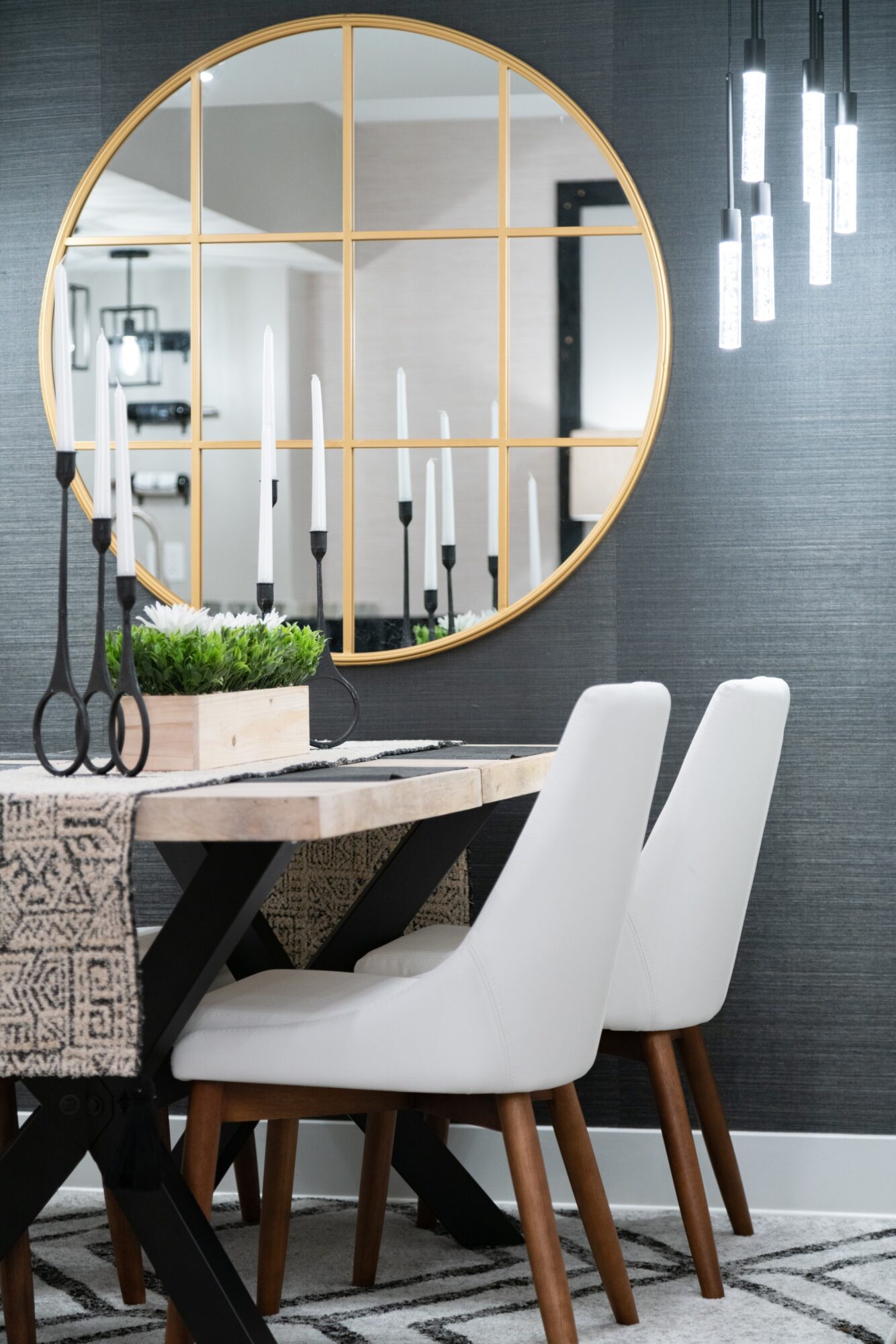 Modern dining area with a round mirror, white chairs, and a table with a plant and hanging scissors, gray wall background.