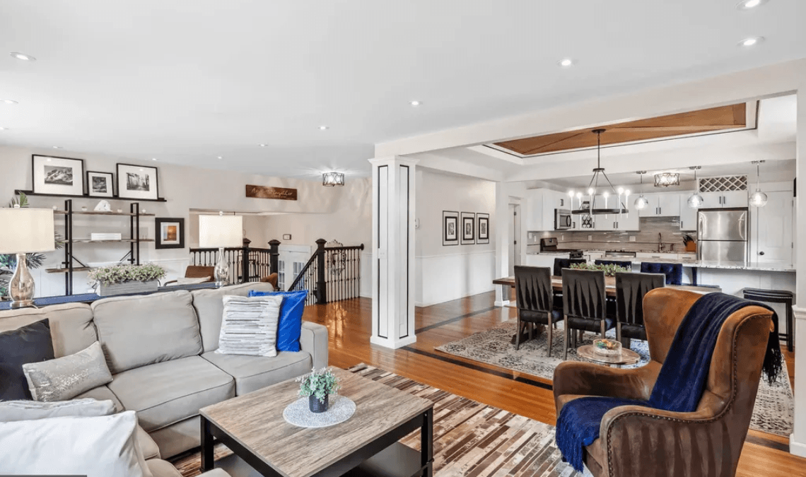 Living room with gray sofa, armchair, coffee table, and open kitchen with dining area, hardwood floors, and modern decor.