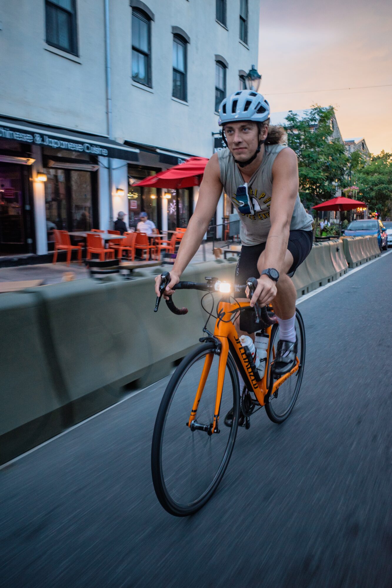 Man riding a yellow bicycle on a city street during evening, with outdoor seating and buildings in background.