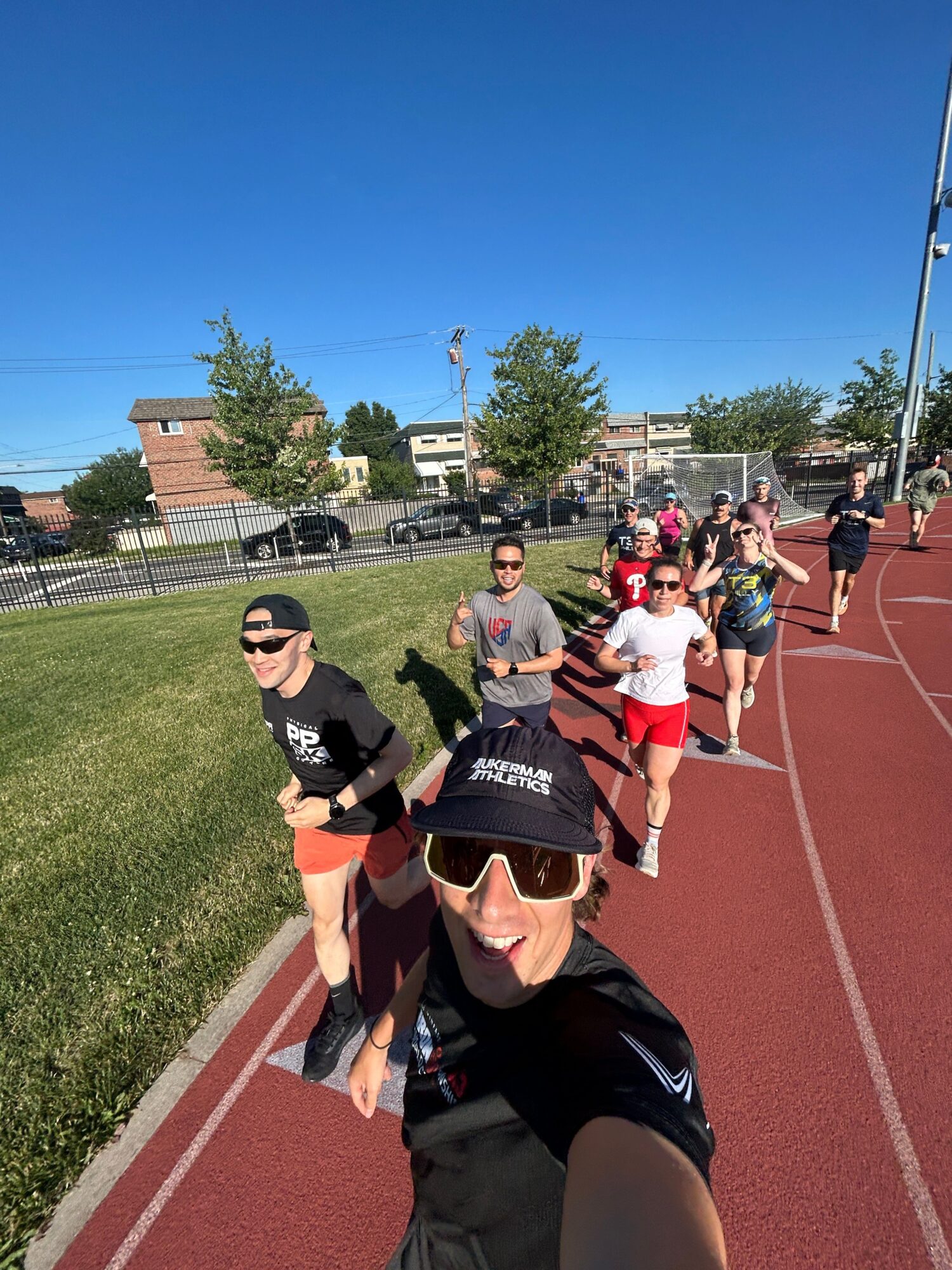 Group of people walking on a red running track outdoors, with blue sky and trees in the background.