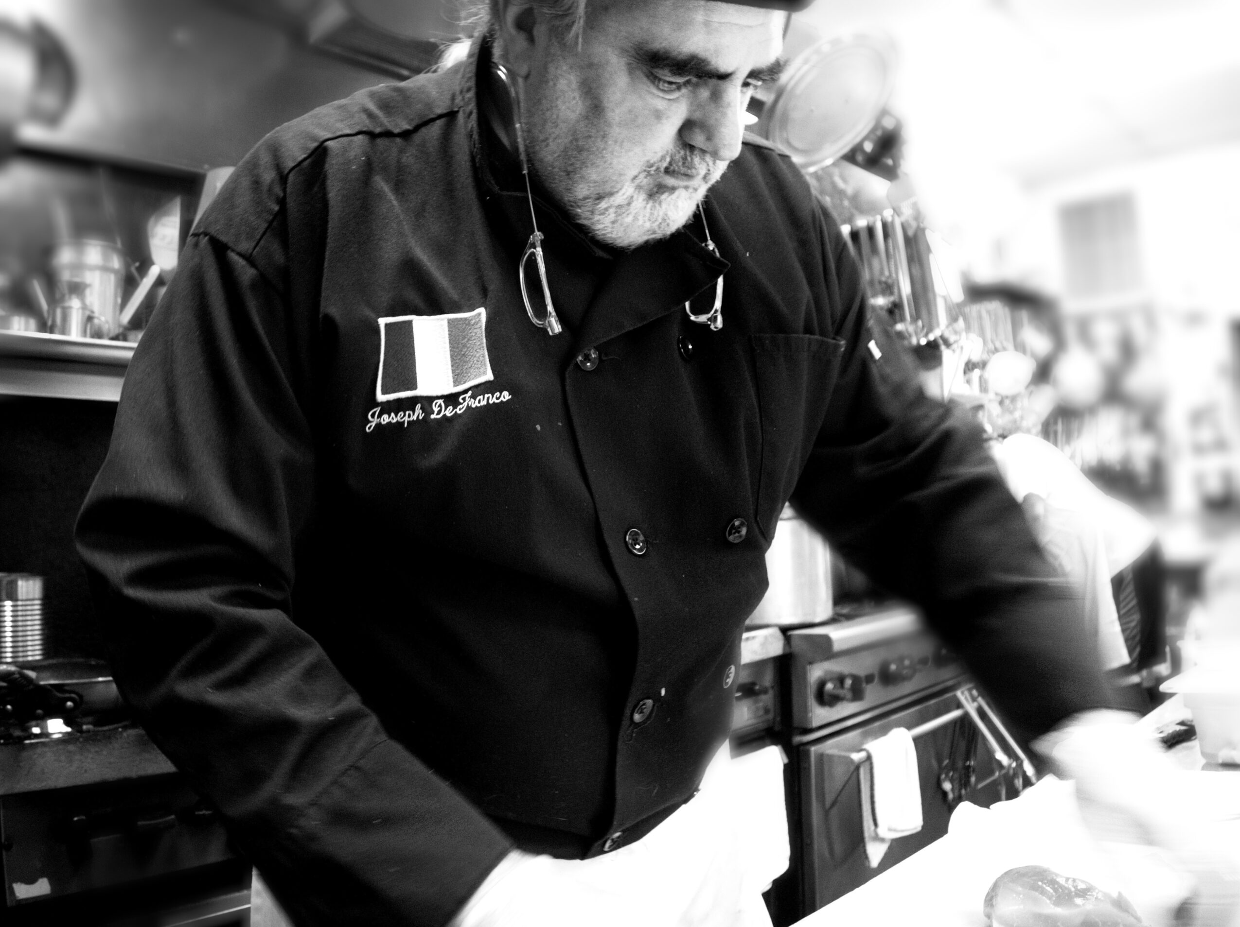 Man in chef's uniform working in a kitchen, focused on his task, black and white photo.