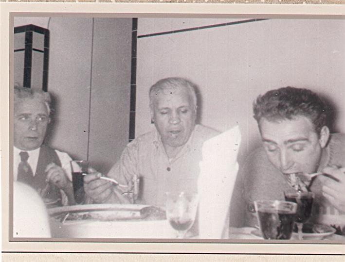 Three people sitting at a table, eating and drinking, in a black-and-white photo.