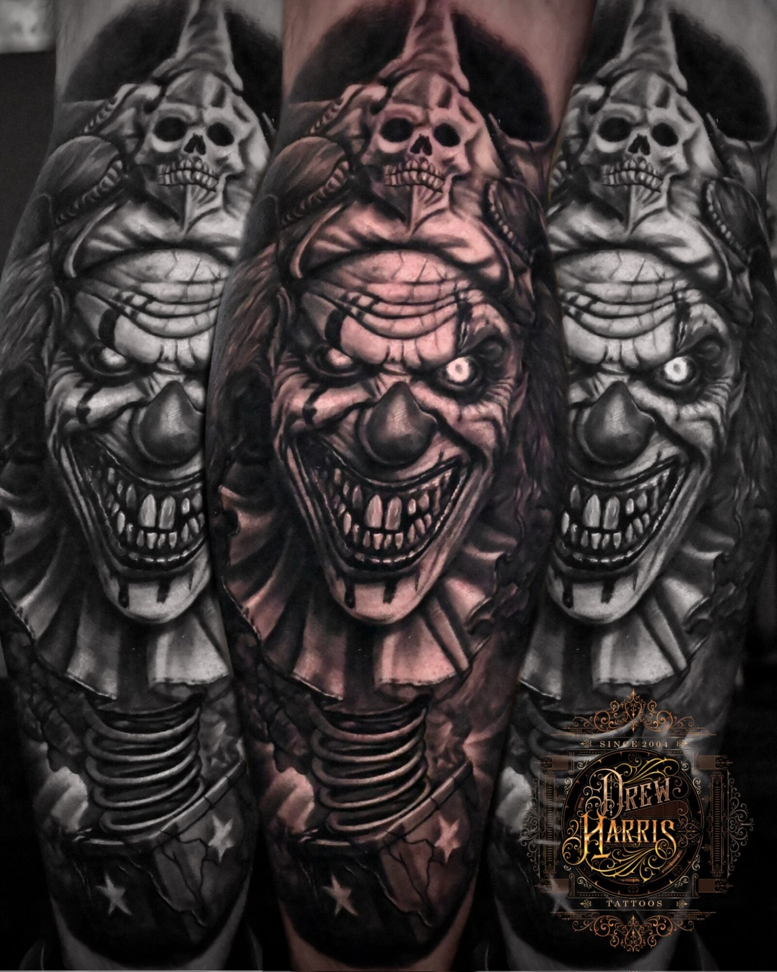 Tattoo of a sinister clown with a skull on its forehead, sharp teeth, and intense eyes, in black and gray shading.