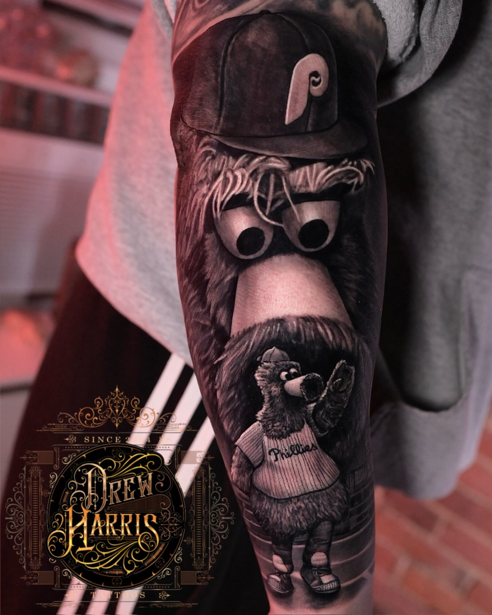 Person's arm with detailed black and gray tattoo of a dog wearing a hoodie and sunglasses, with a patch on the sleeve.