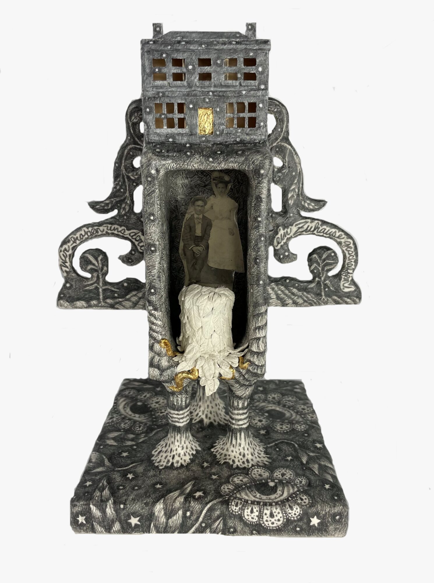 Decorative sculpture with a central figure, surrounded by intricate patterns and structures, resembling a stylized building or shrine.