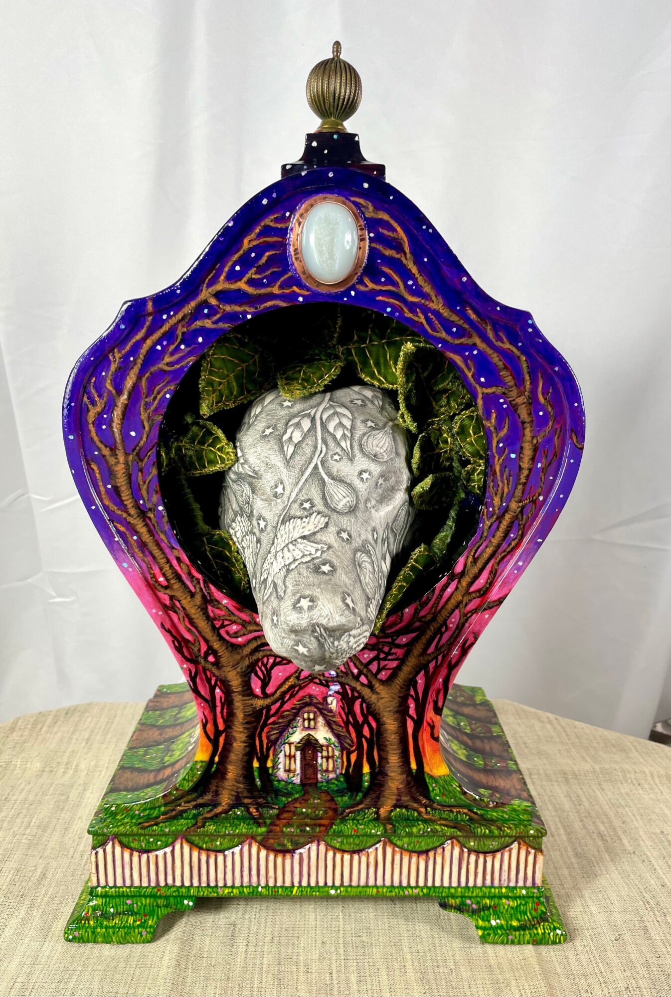 Decorative box with a tree and face design, featuring a purple top, green base, and intricate details.
