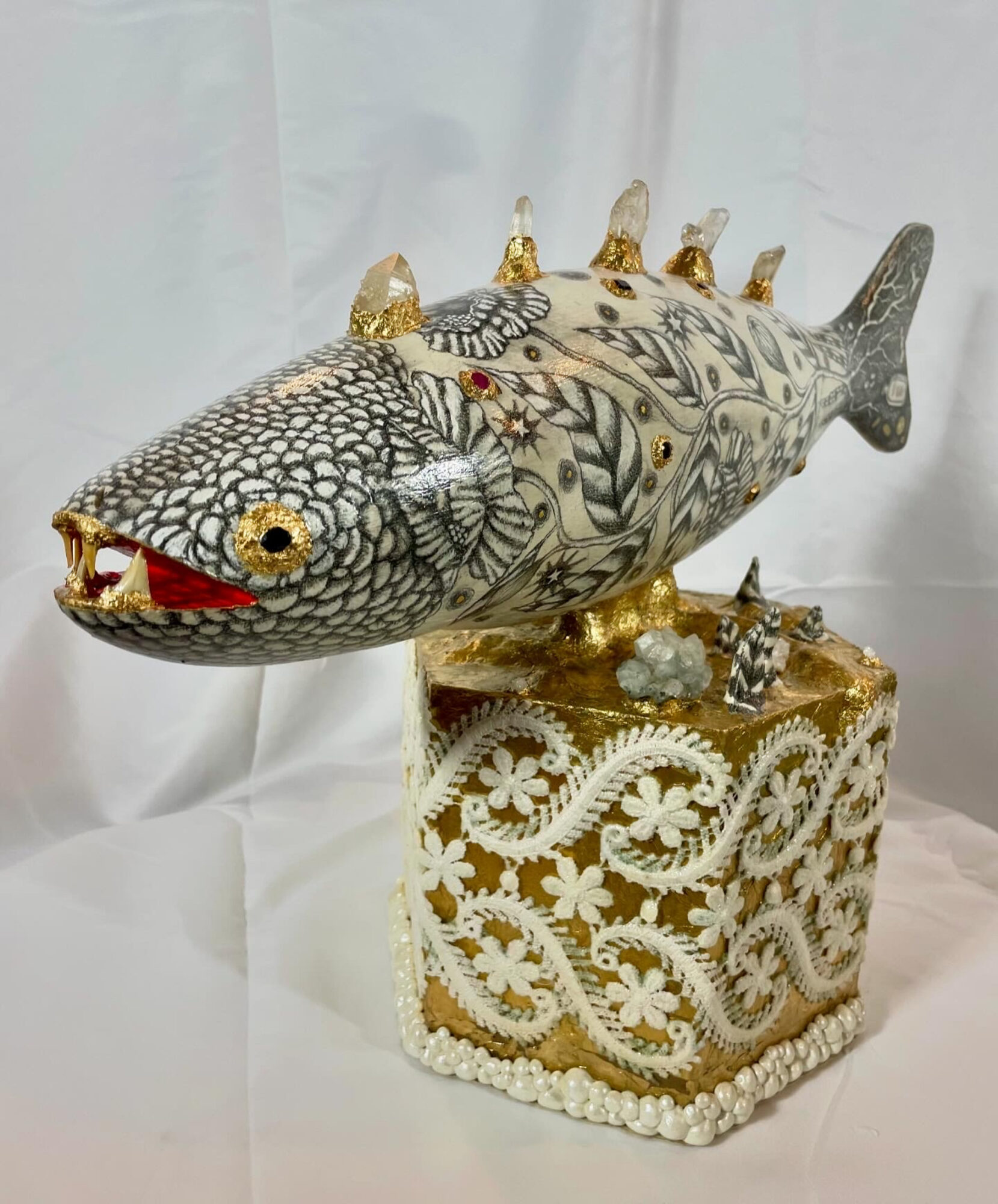 Decorative fish sculpture with intricate patterns, mounted on a ornate gold and white base, against a white background.