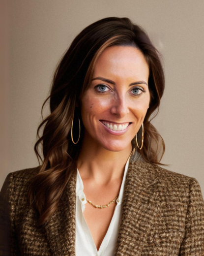 Woman with long wavy brown hair, wearing hoop earrings, a white blouse, and a brown blazer, smiling.