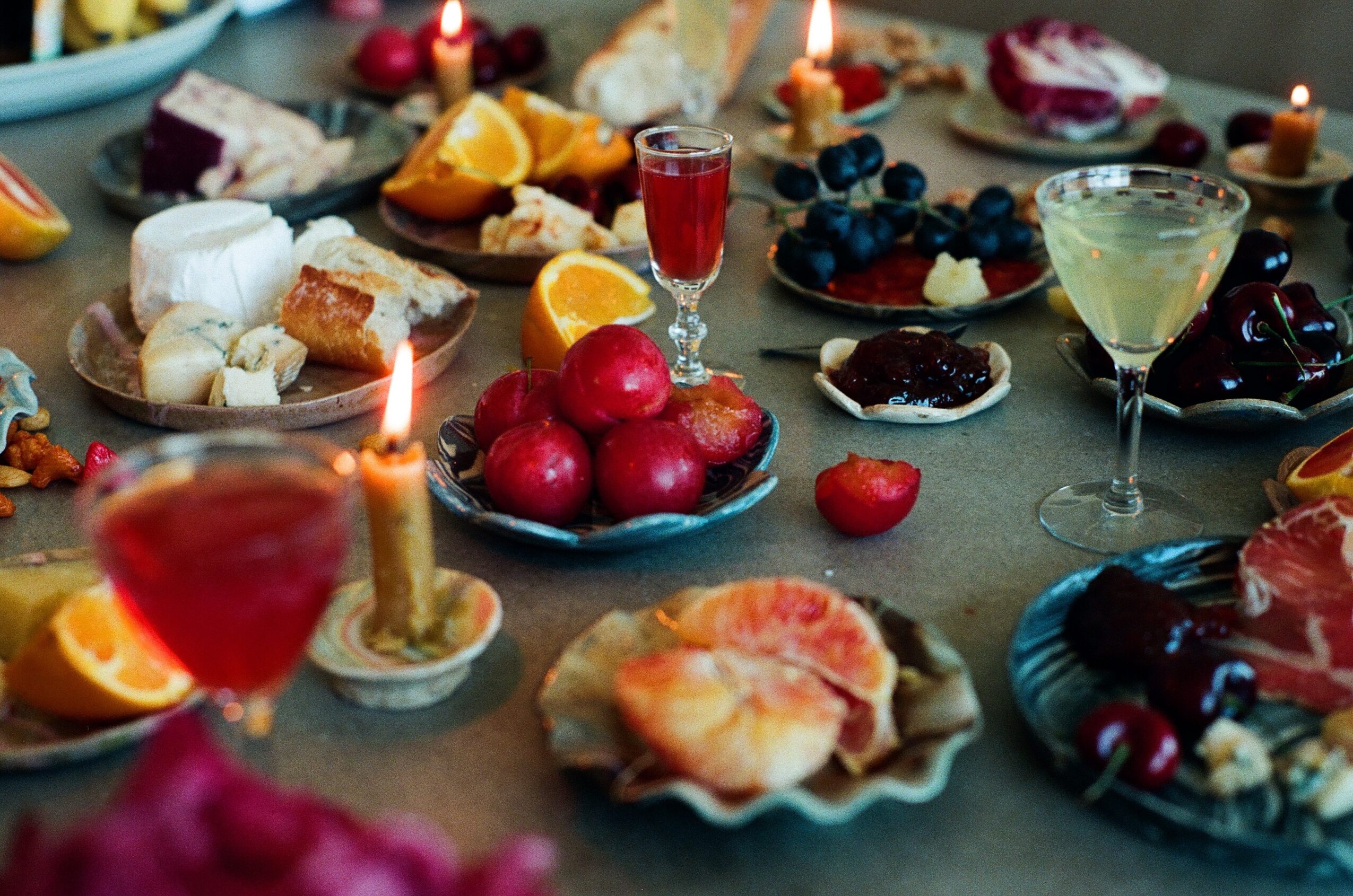 Table with various desserts, fruits, candles, and drinks arranged for celebration or gathering.