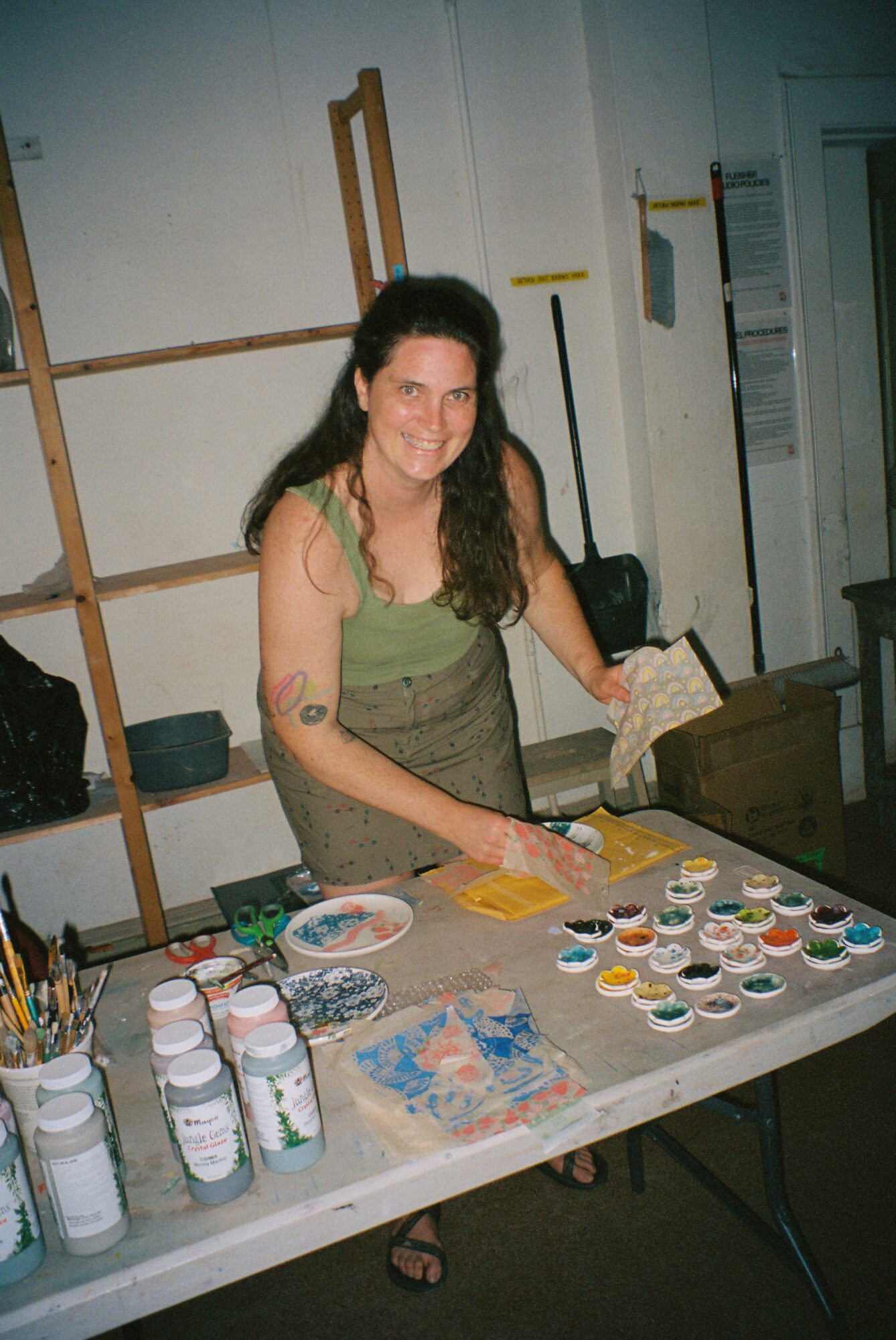 Woman with long dark hair leaning over a table with paint supplies, in a room with white walls and wooden beams.