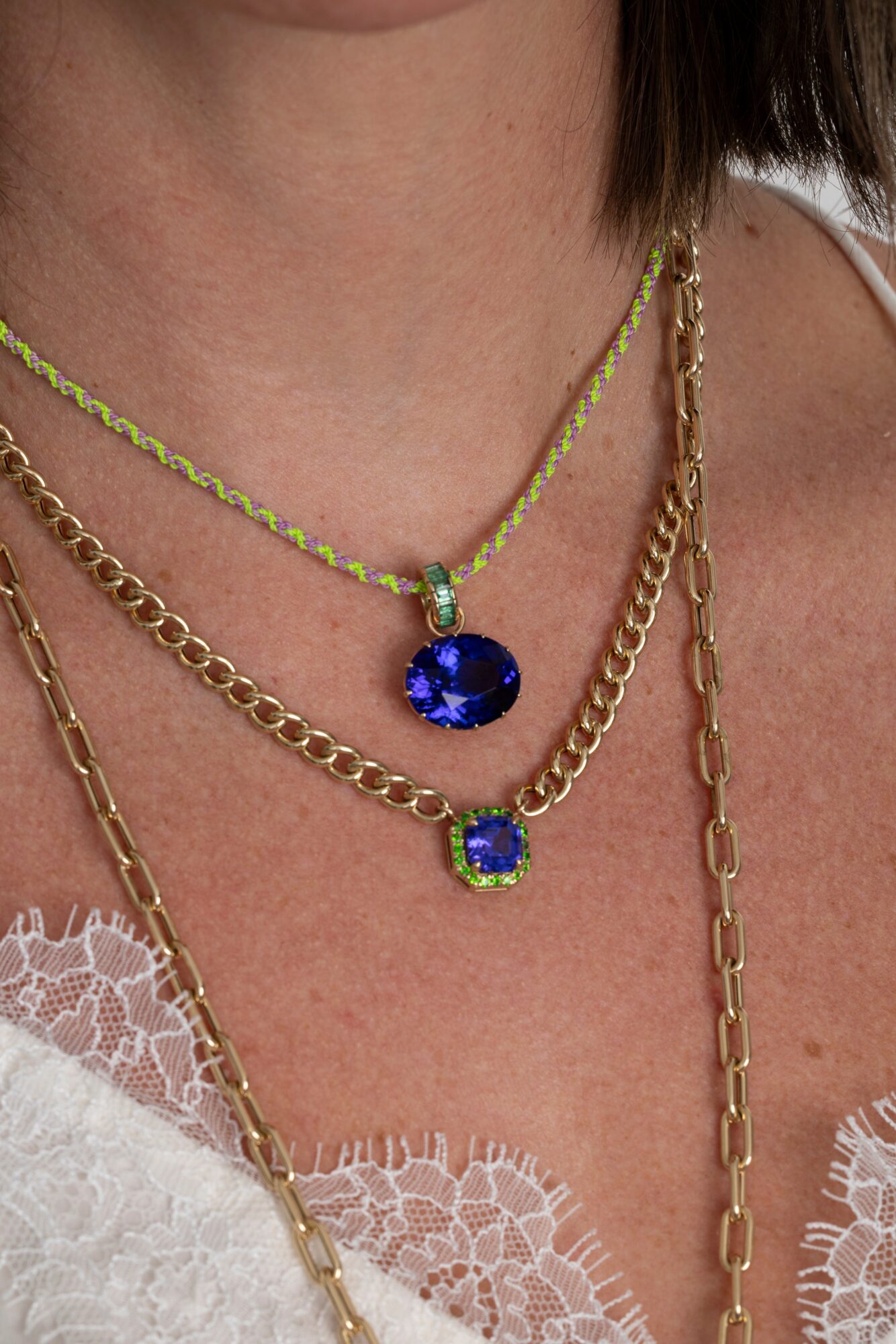 Close-up of a person's neck with layered necklaces, including a blue pendant and gold chains, over a lace top.