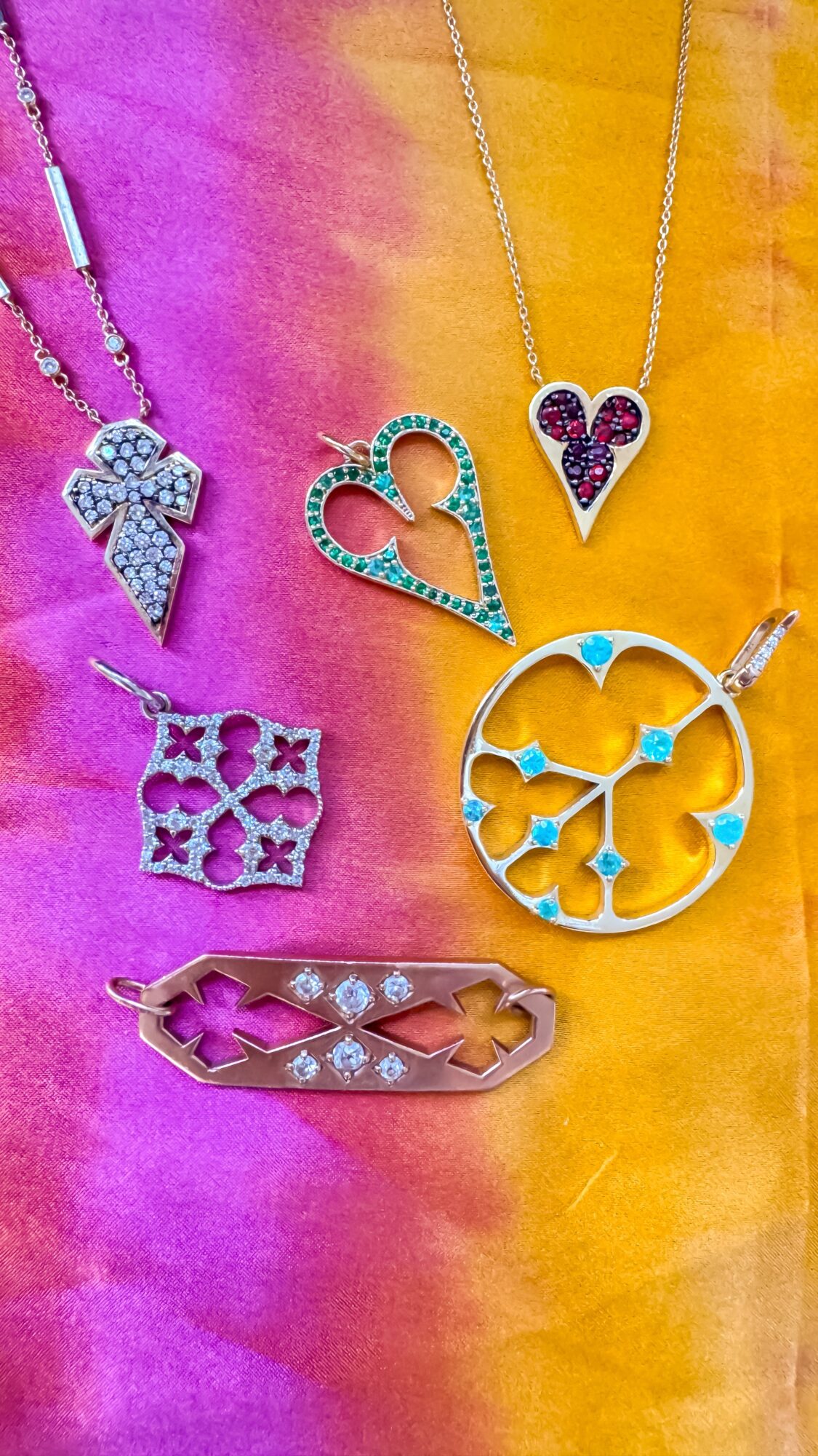 Six pieces of jewelry including necklaces and rings with heart and bow designs, displayed on a colorful fabric background.