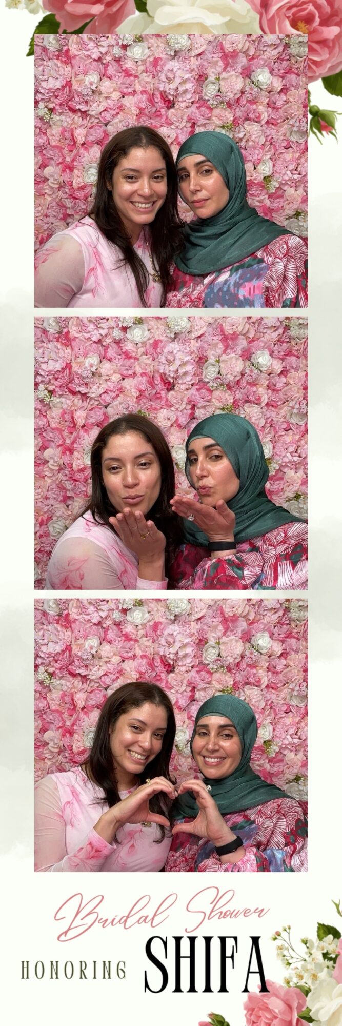 Two women smiling and making a heart shape with their hands in front of a pink floral background.