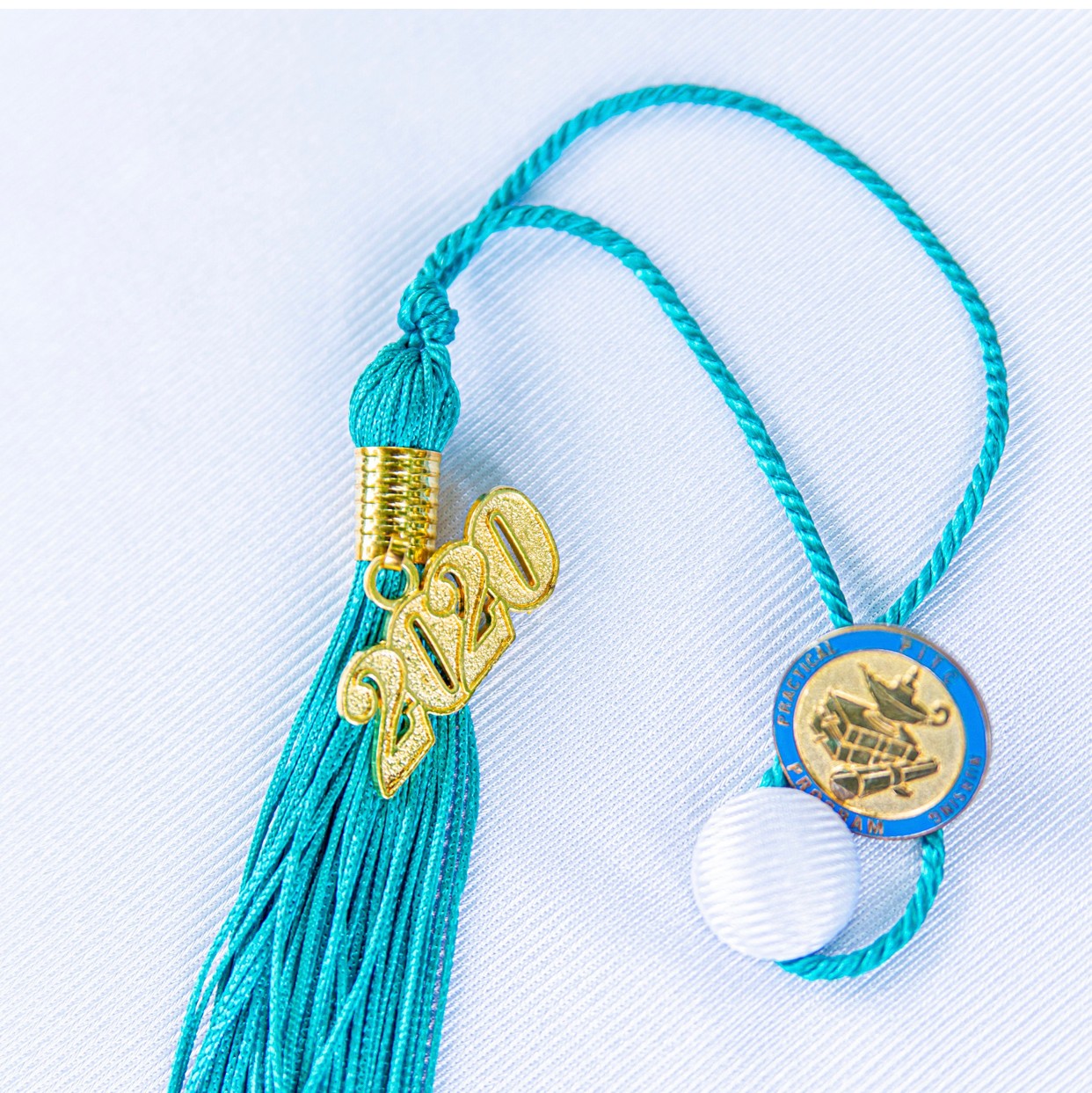 Blue tassel with gold '2020' charm, blue cord, and circular medallion with boat image, on light background.