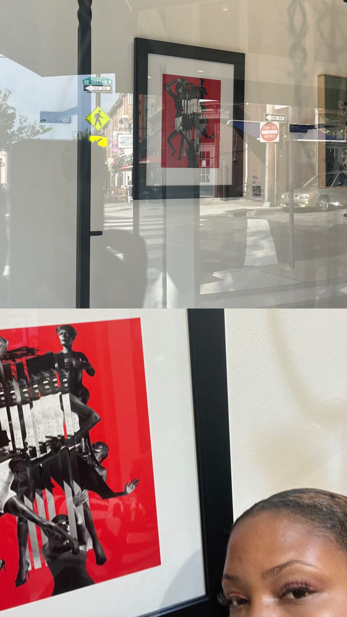 Framed artwork on a wall viewed through a glass window, with reflections of street signs and buildings outside.
