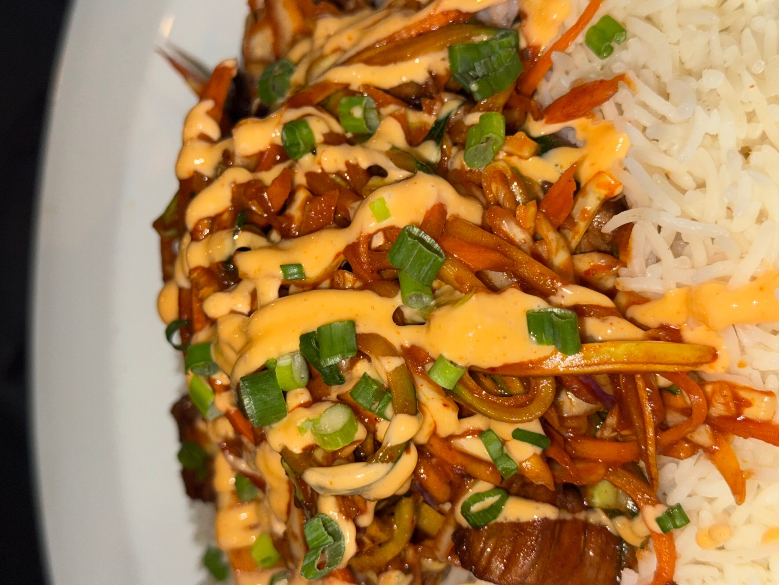 Stir-fried vegetables with sauce and chopped green onions next to white rice on a plate.