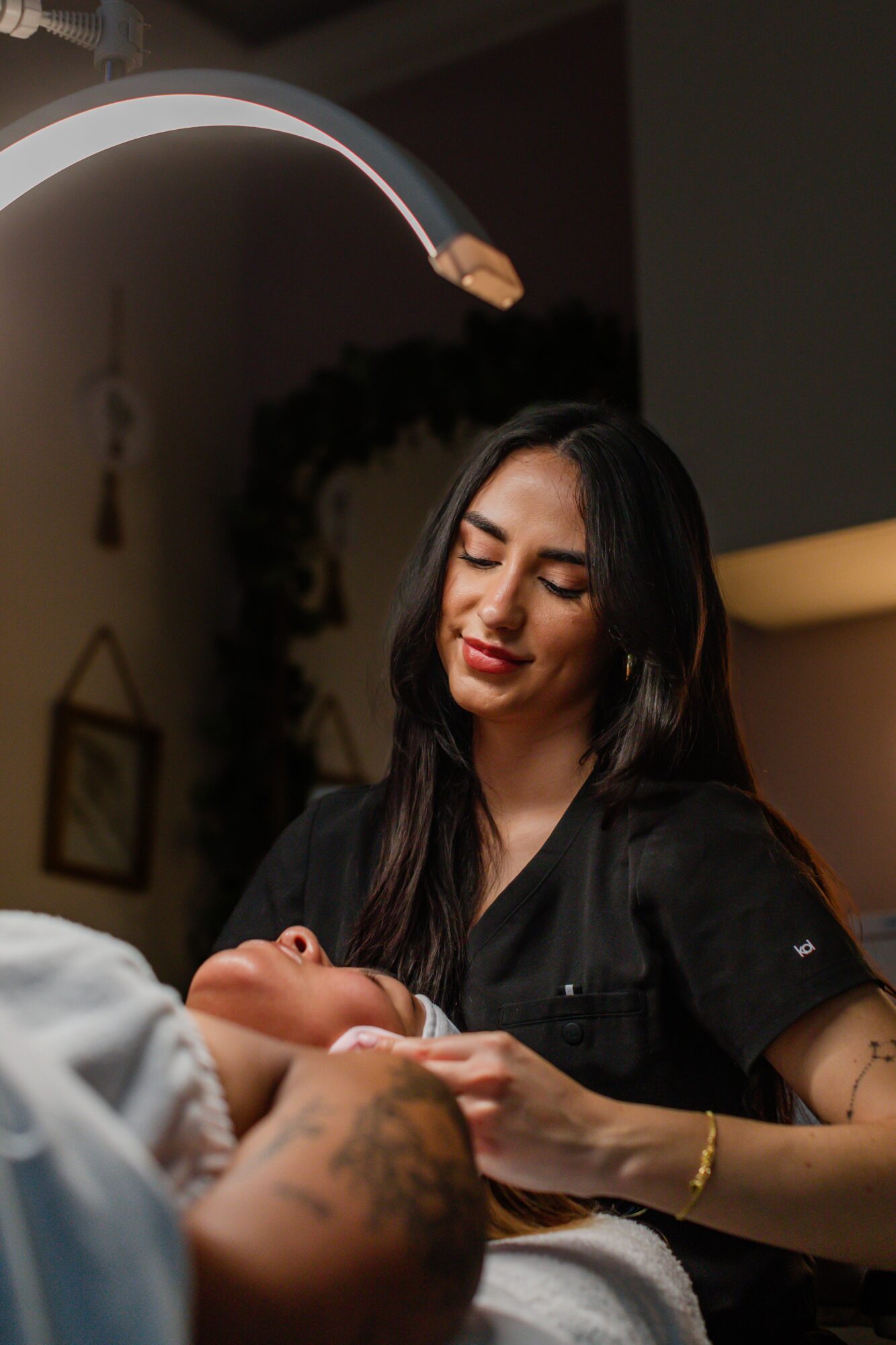 A woman with long dark hair and a black uniform looks at a newborn baby in a clinical setting.