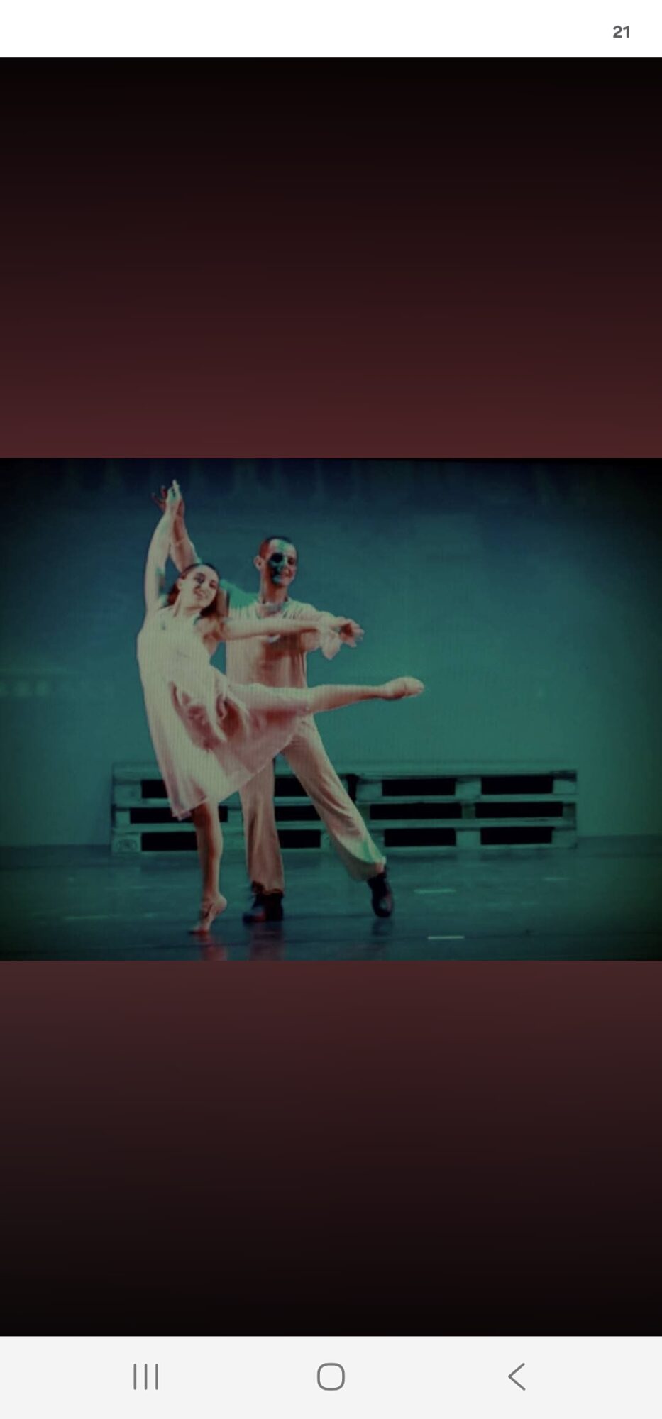 Two ballet dancers perform on stage, one lifting the other, with a dark background and stage props.