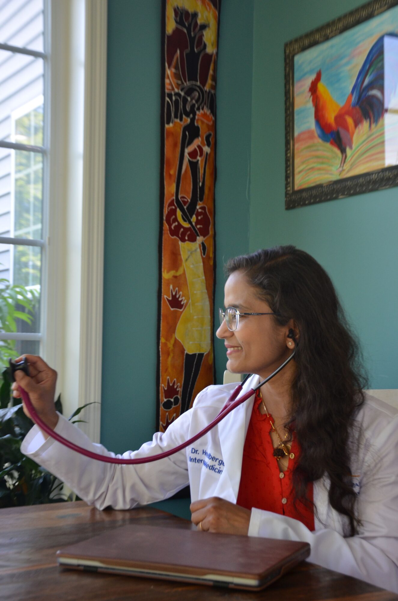 Girl lying on her side, holding a stethoscope to her ear, looking at it, near a window and colorful painting.