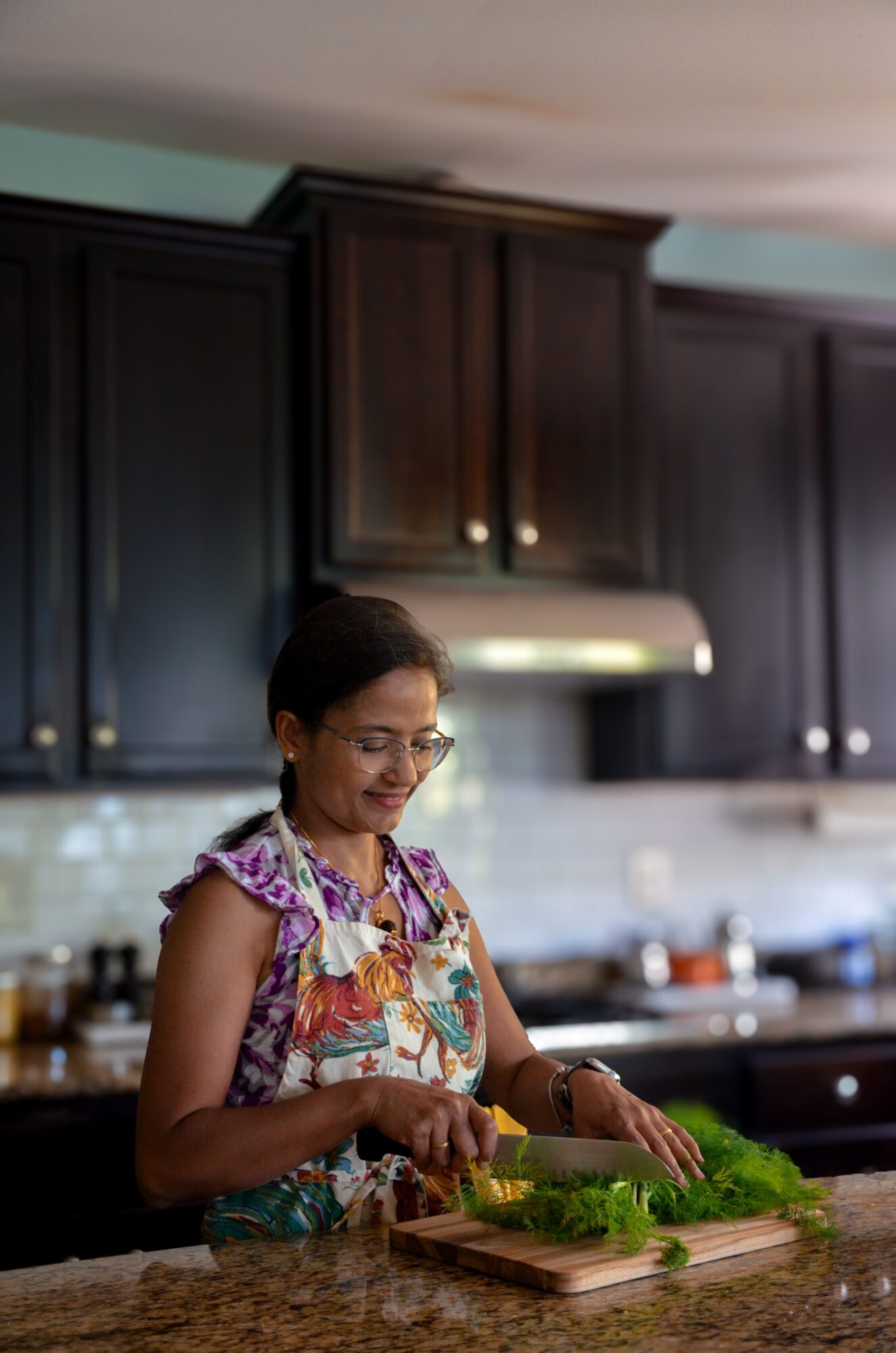 Woman wearing an apron chopping vegetables in a kitchen with dark cabinets and a range hood