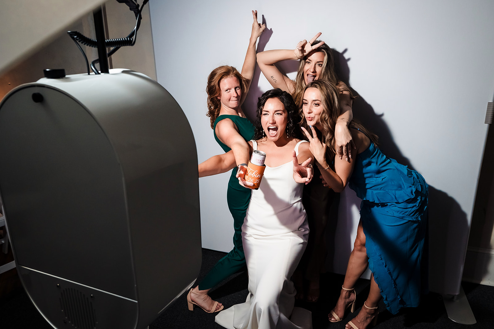 Four women celebrating and taking a selfie together, smiling and making gestures, in a photo studio setting.