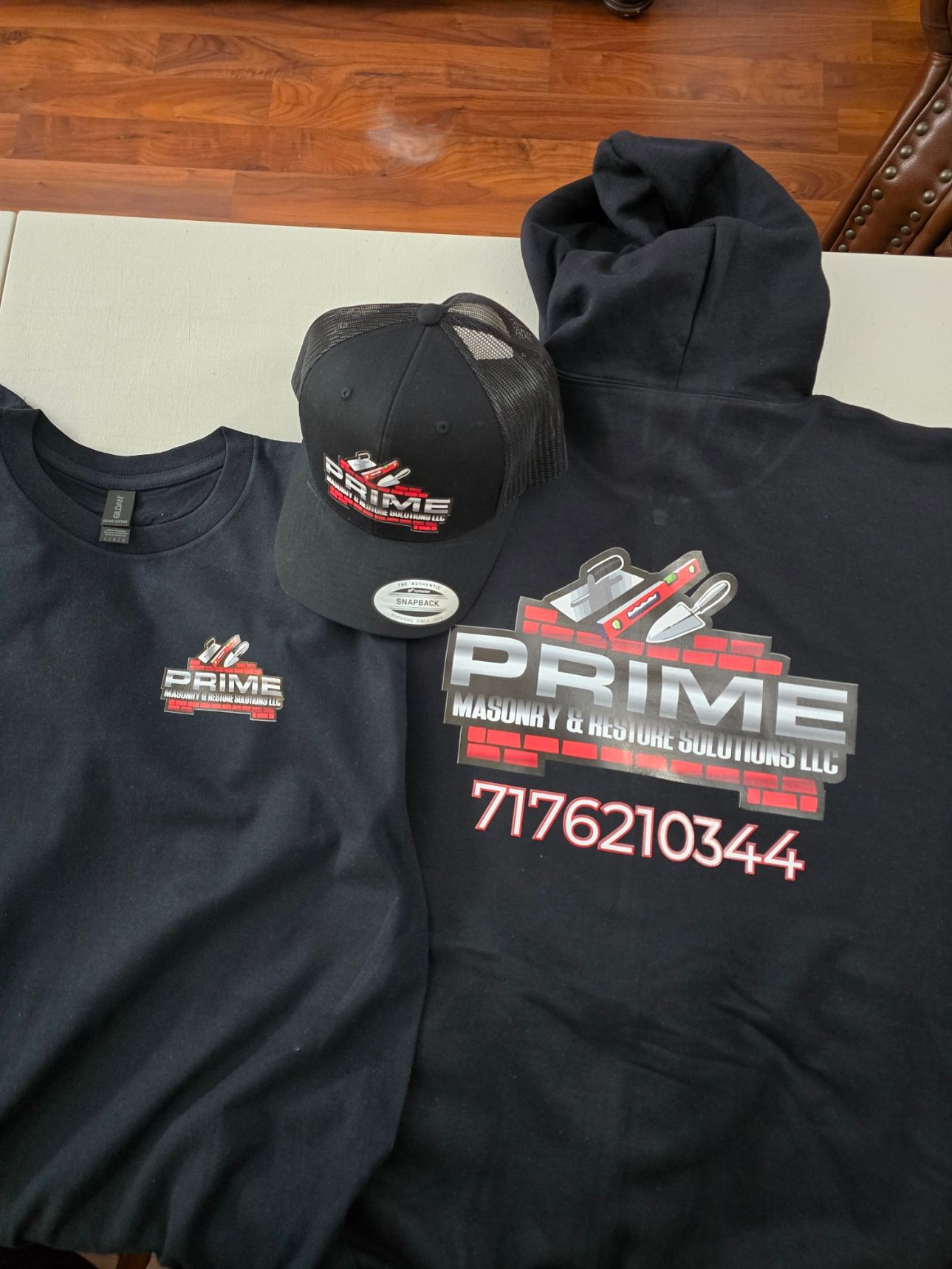 Black hoodie and navy vest with racing logos and text, cap with logo, on a table.