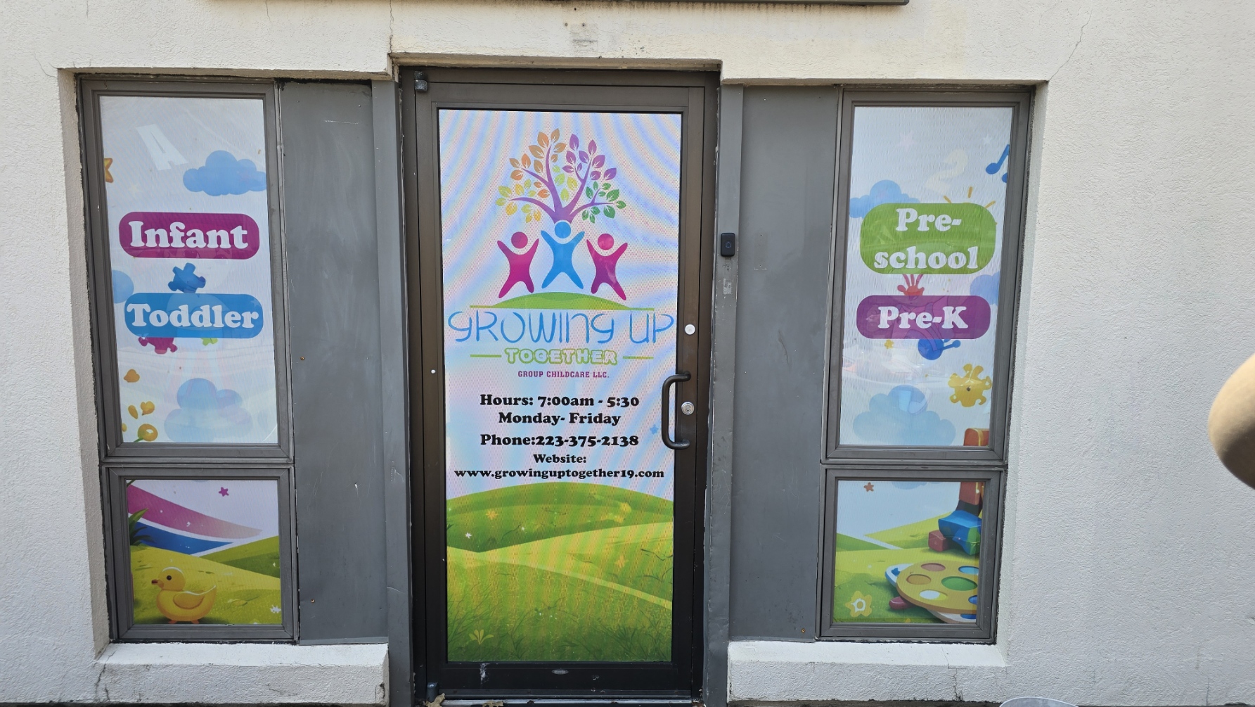Door with colorful sign and windows displaying children's educational themes, including a tree and outdoor scenes.