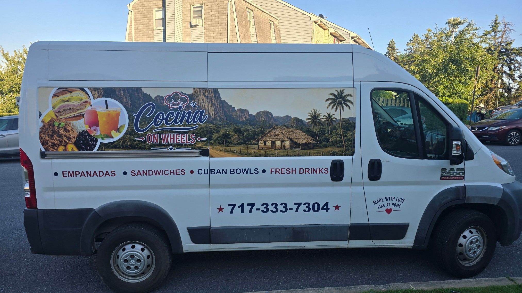 Side view of a white food truck with colorful graphics and text advertising Cuban cuisine, phone number, and menu items.