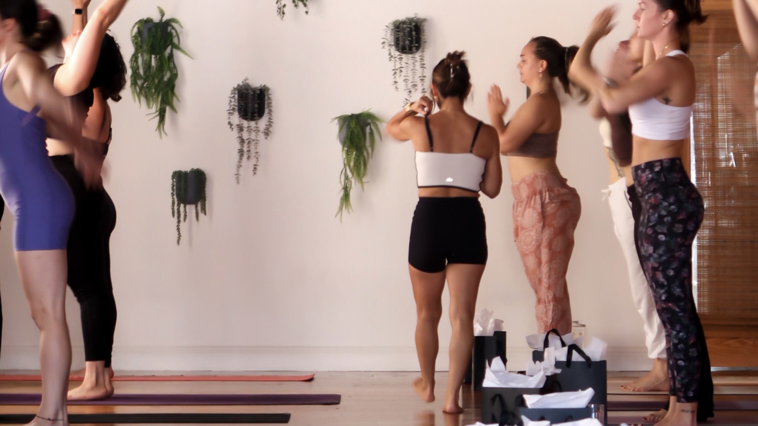 Group of women participating in a fitness class in a bright room with plants on the wall.