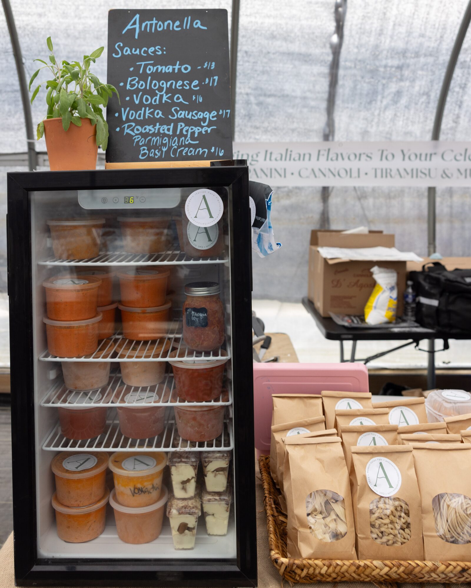 Display case with food containers, a chalkboard menu, and paper bags on a table in a bright setting.