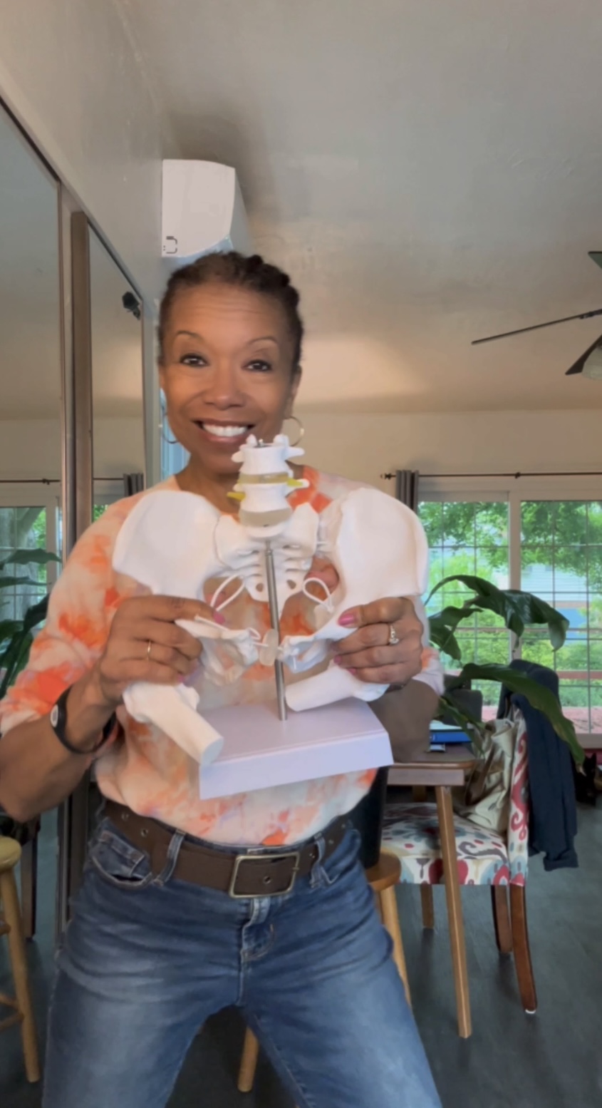 Woman holding a decorated cake with a smiling expression, standing indoors near a window and dining table.