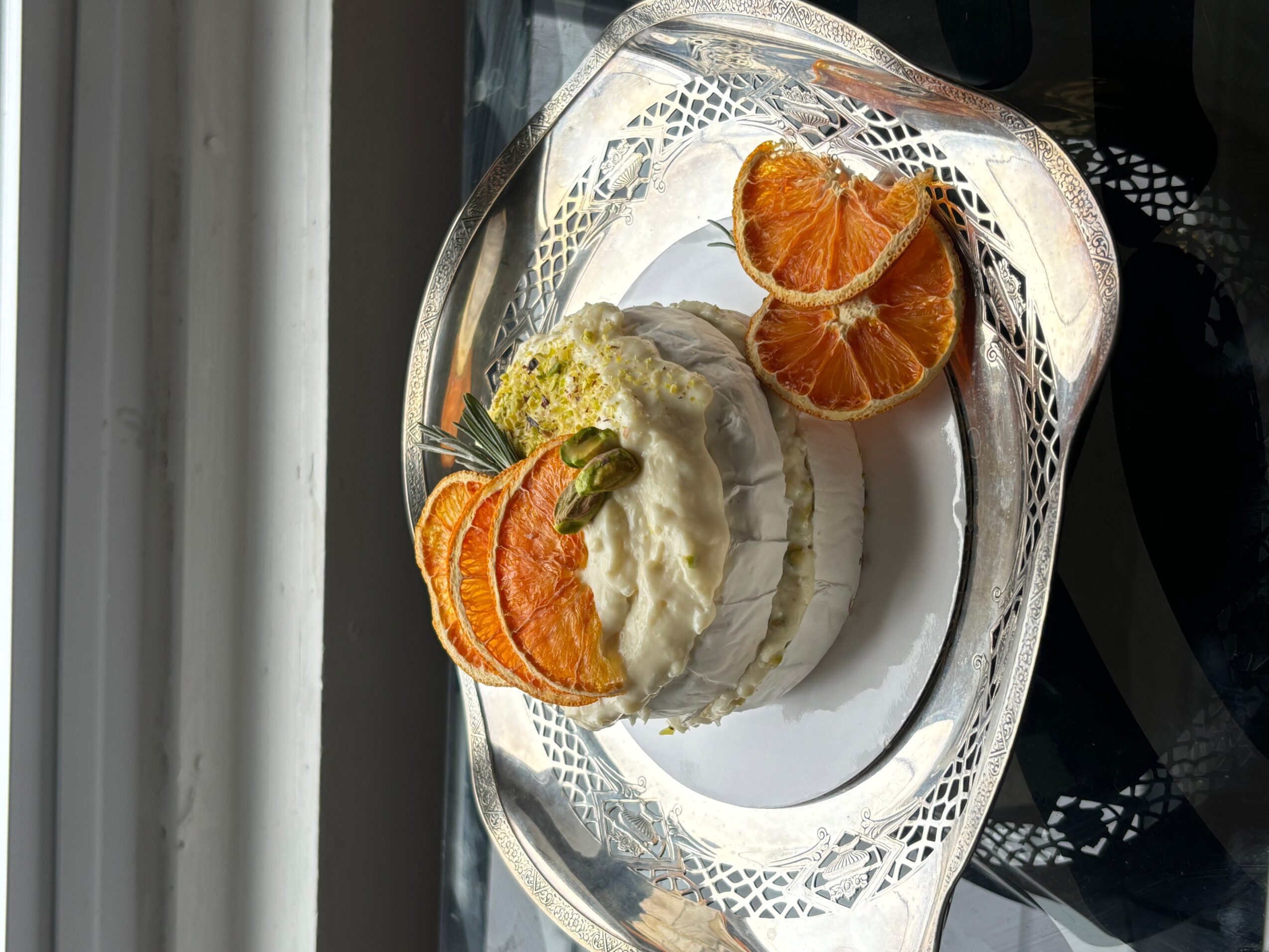 Sliced oranges and a dessert with cream and fruit on a decorative glass plate.