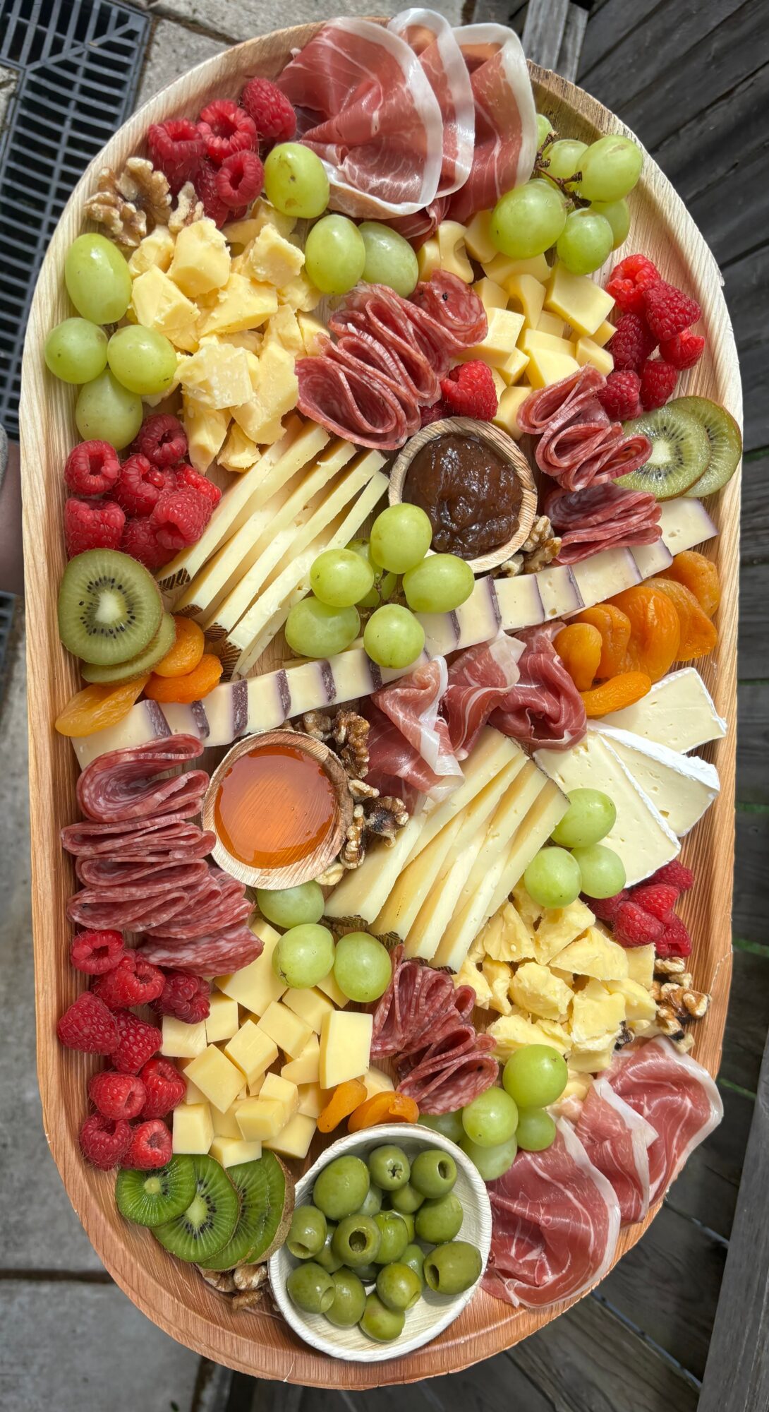 Assorted cheese, grapes, sliced meats, kiwi, and raspberries on a platter.