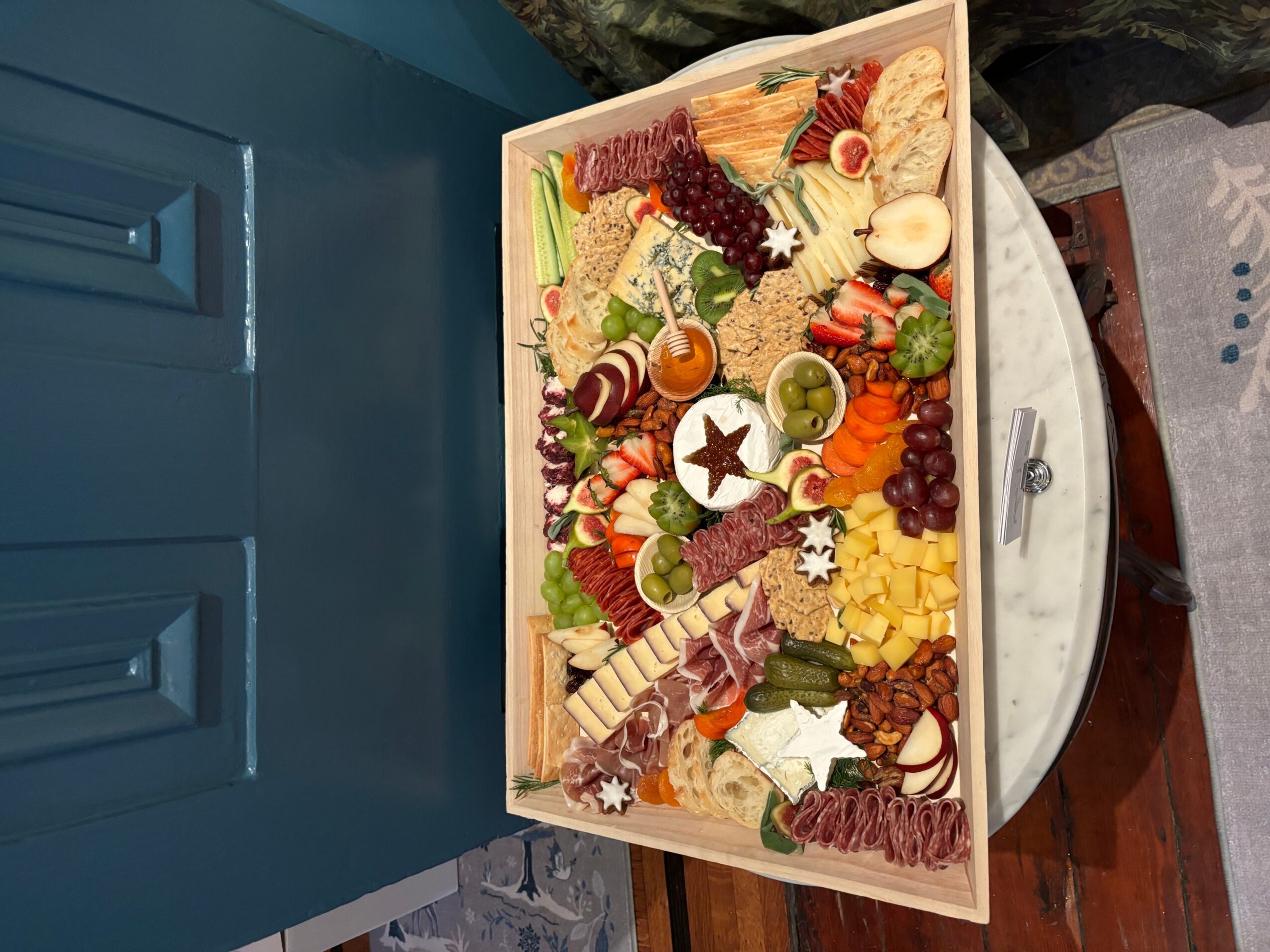 A wooden tray filled with assorted cheeses, grapes, and crackers on a table.