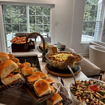 Table with sandwiches, salad, and a bowl of chips in a bright room with large windows and outdoor view.