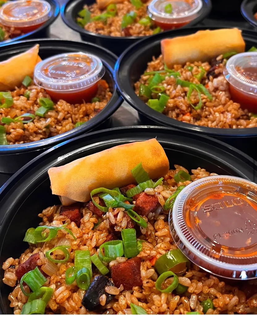 Multiple black bowls filled with fried rice, topped with spring onions, a spring roll, and a small container of sauce.
