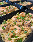 Containers filled with shrimp pasta garnished with chopped green onions and black sesame seeds.